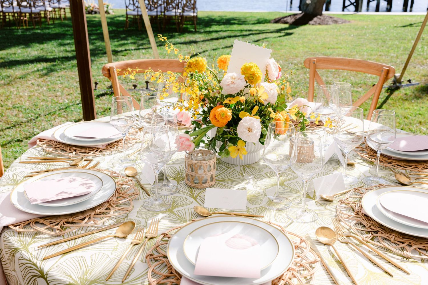 Elegant round table setting with yellow and white floral centerpiece and gold accents.