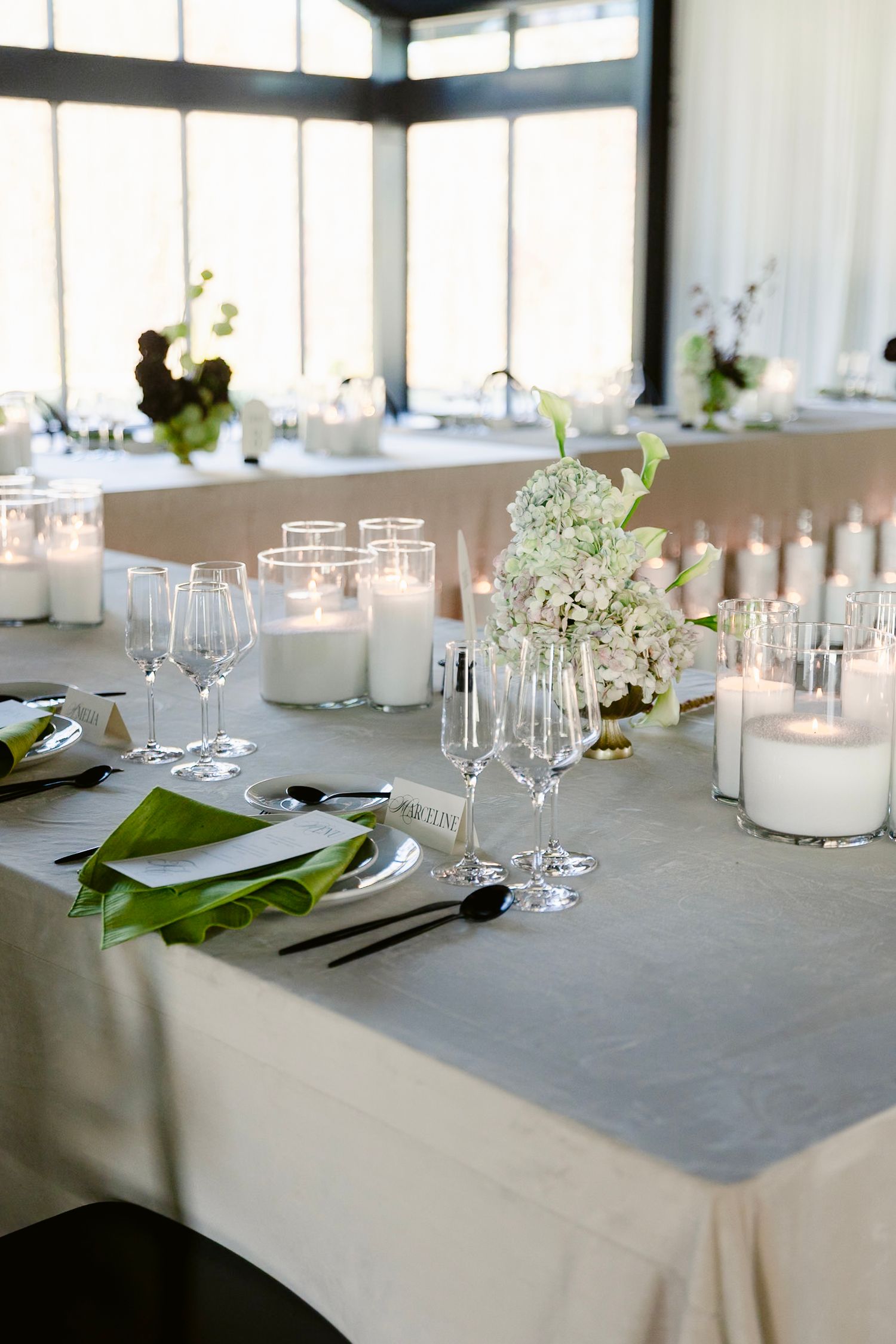 Modern wedding reception table settings with white linens, glassware, and delicate floral centerpieces create an elegant atmosphere.