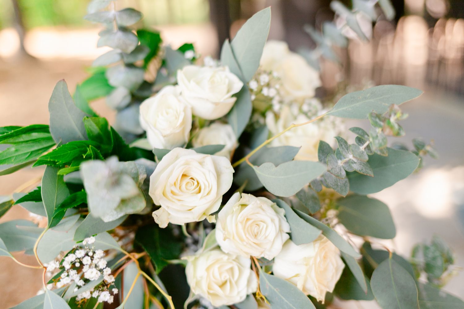 Elegant white roses and eucalyptus leaves arranged in a romantic wedding bouquet with soft bokeh background.