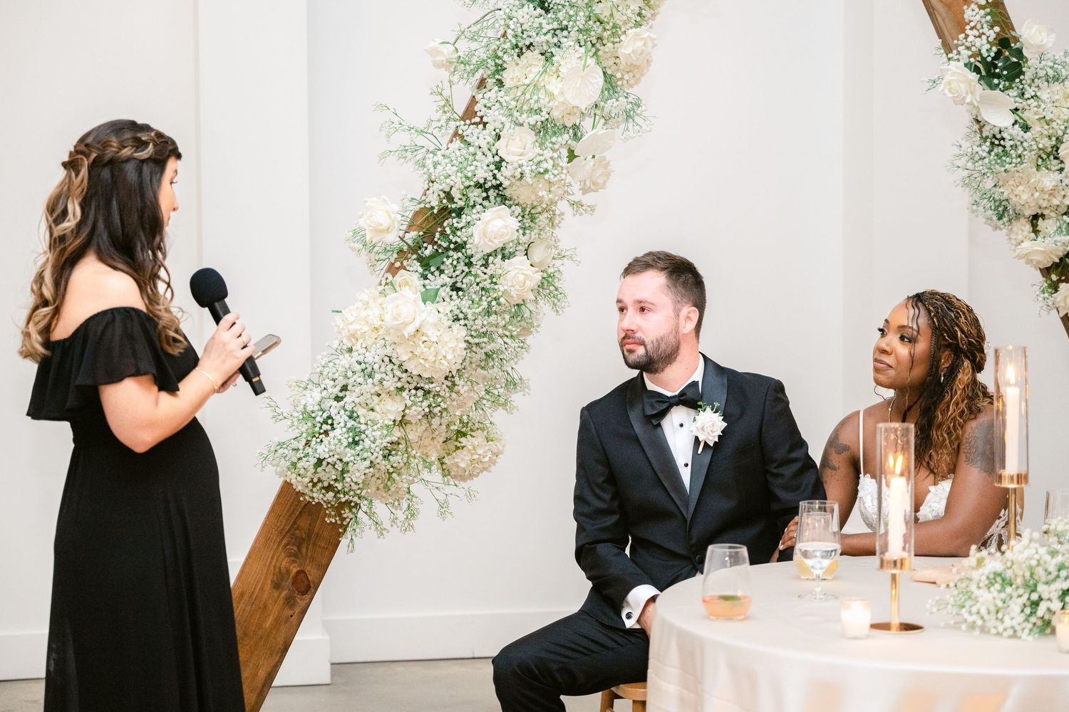 Wedding ceremony taking place in an elegant white room decorated with floral garlands and greenery.