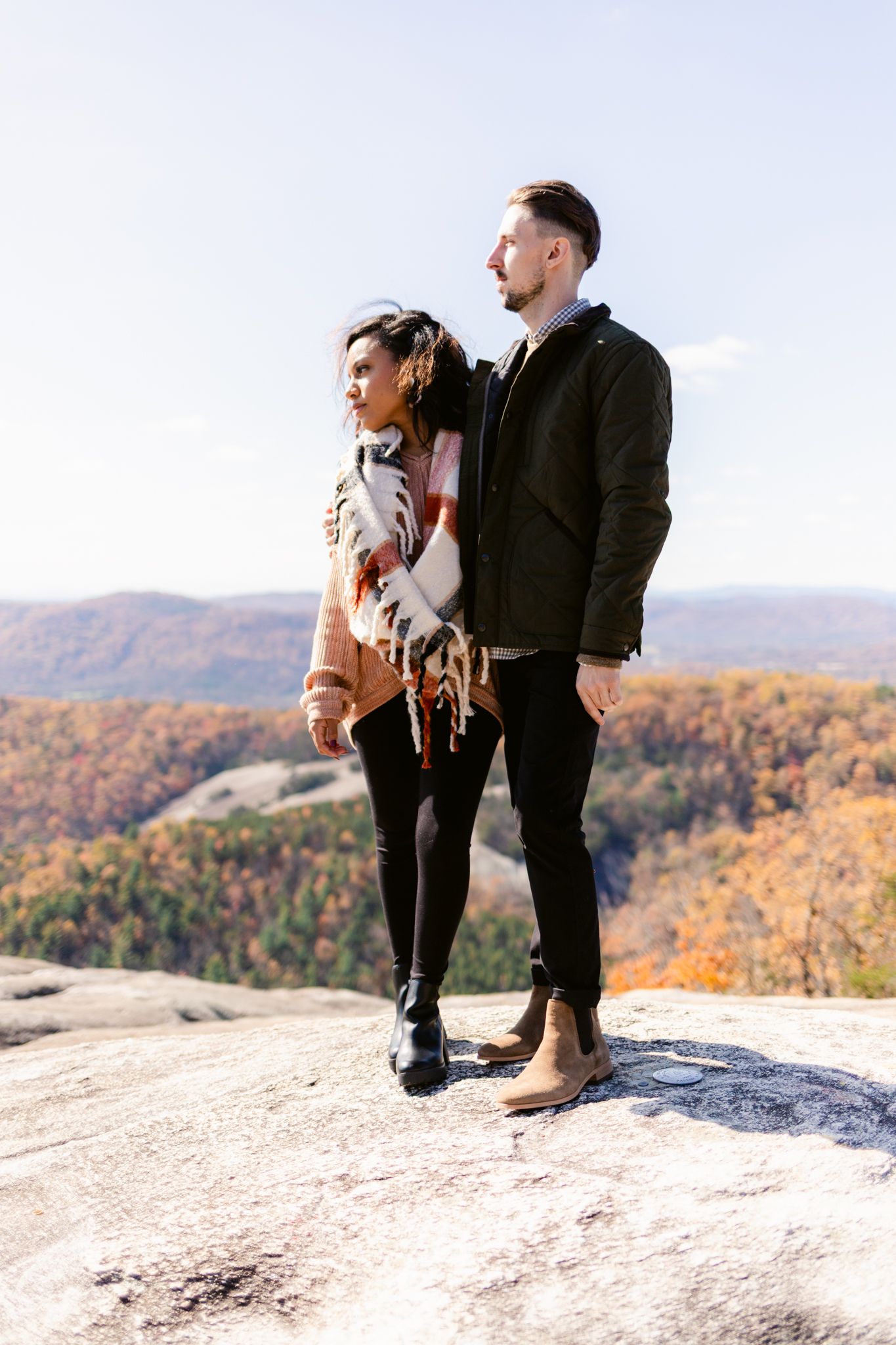 A couple stands on a rocky overlook enjoying scenic autumn mountain views in the distance.