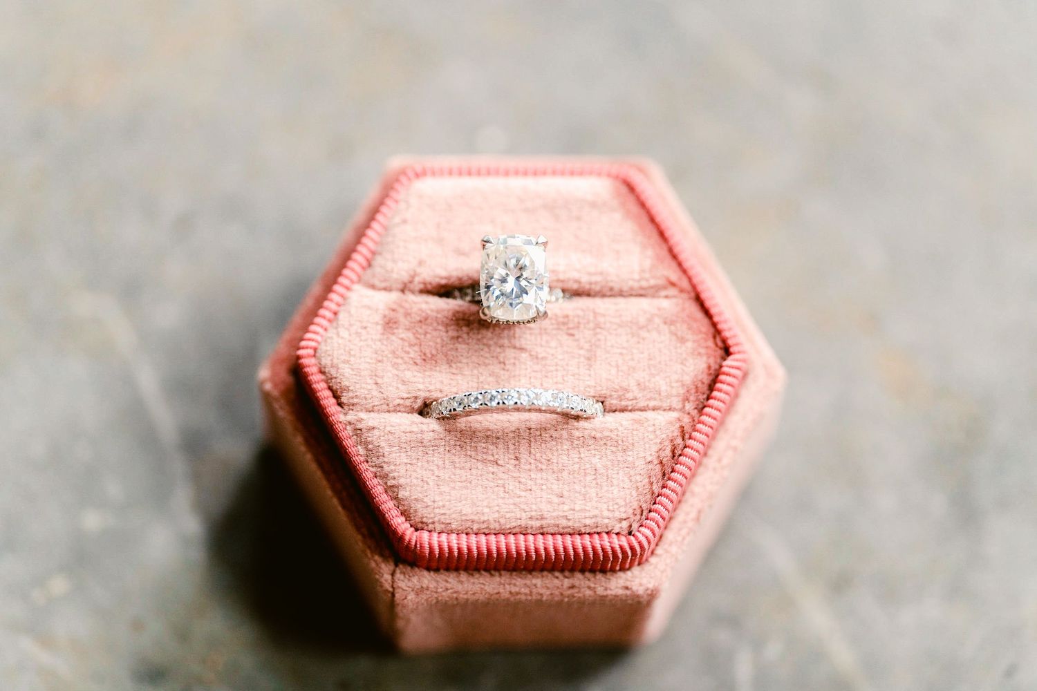 Close-up shots of a pink hexagonal ring box displaying an engagement ring on white fabric.