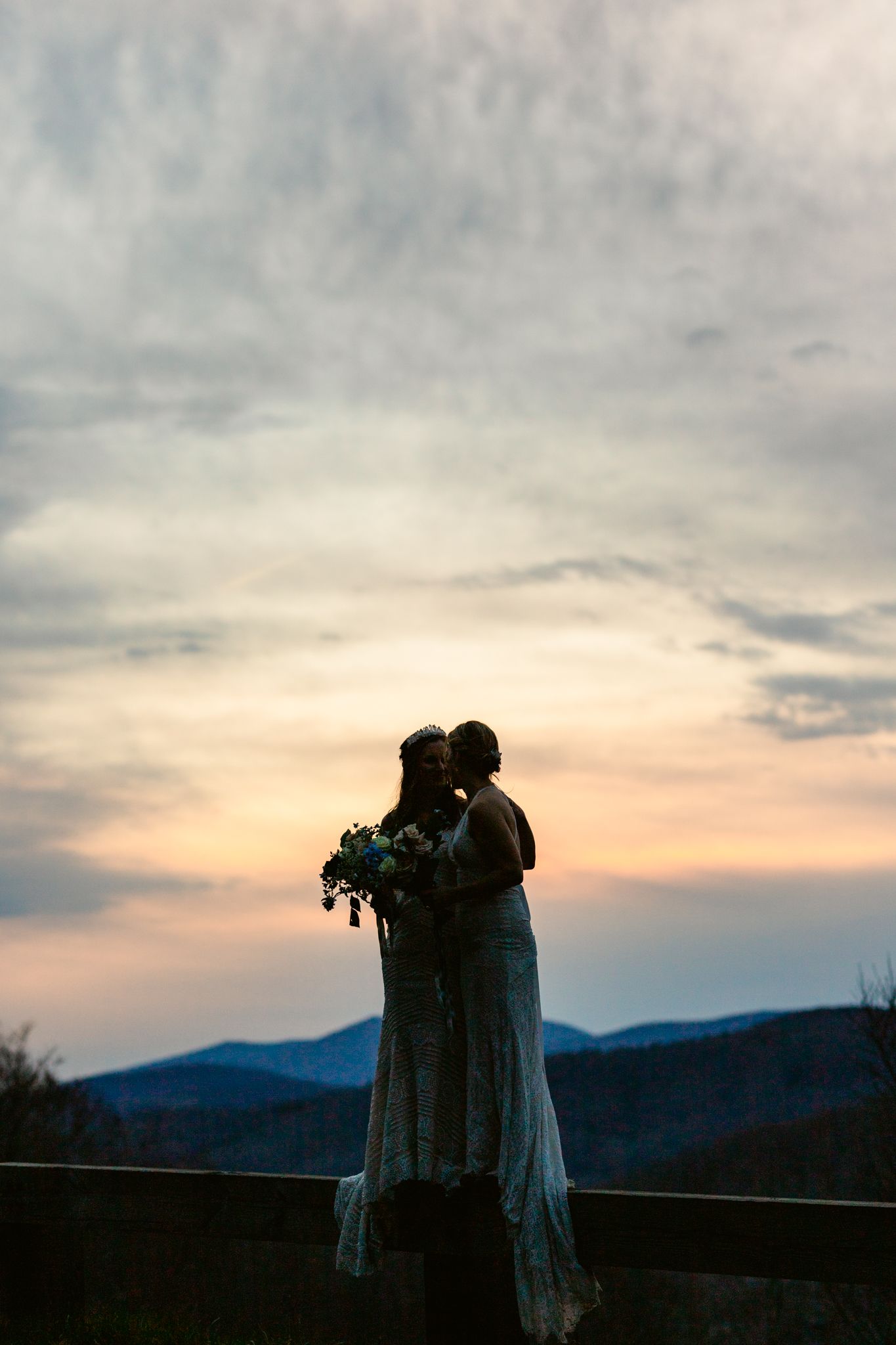 A romantic silhouette of a couple embracing against a mountainous sunset backdrop with cloudy skies.