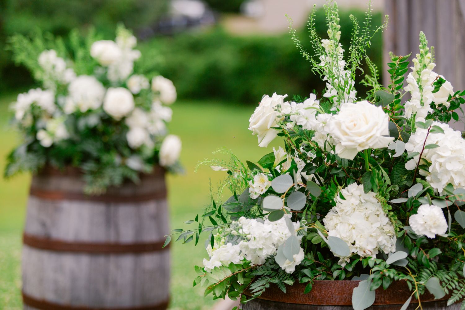 White floral arrangements in rustic wooden barrels create an elegant outdoor garden display.