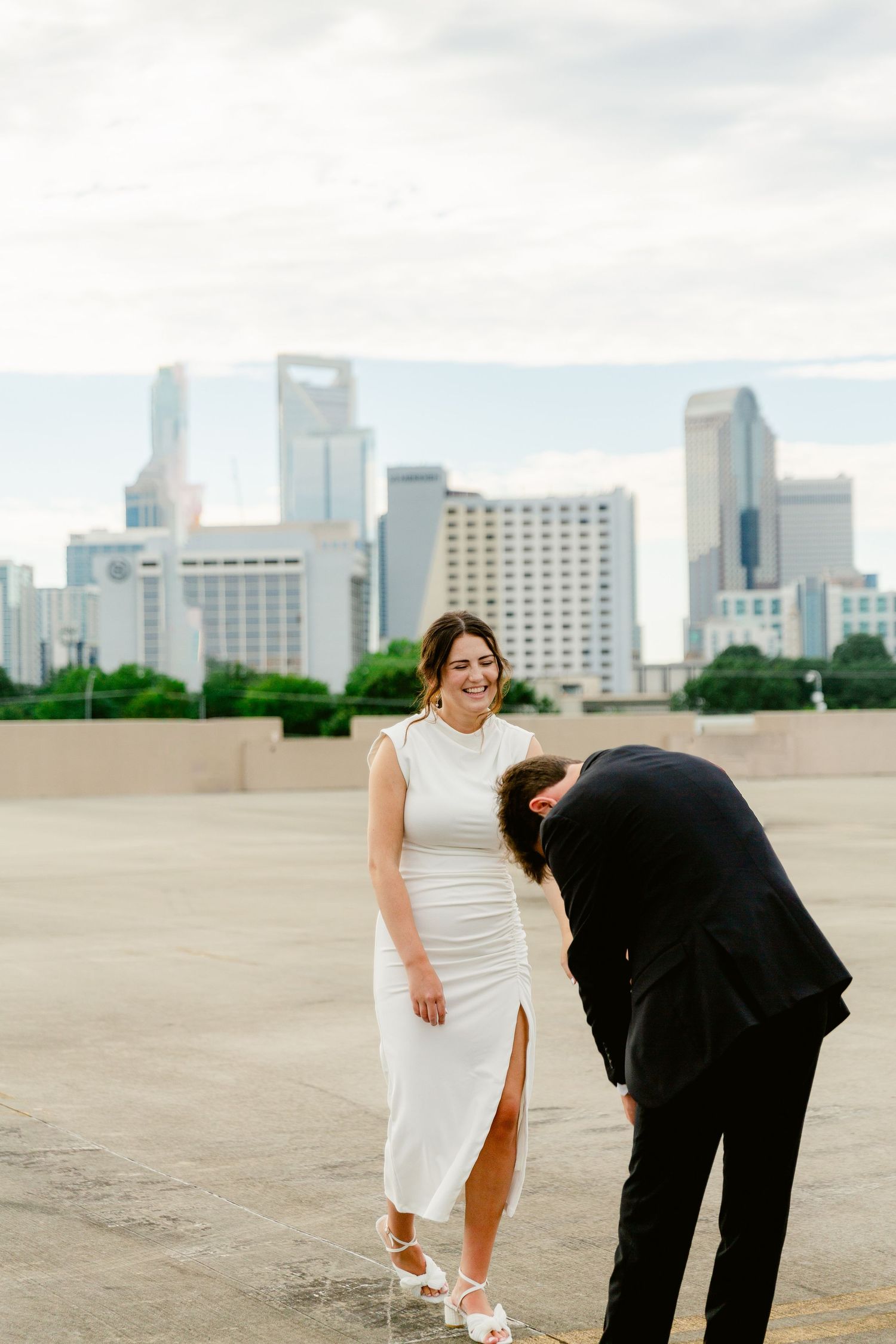 A couple shares a playful moment on an empty rooftop with the downtown Houston skyline in the background.
