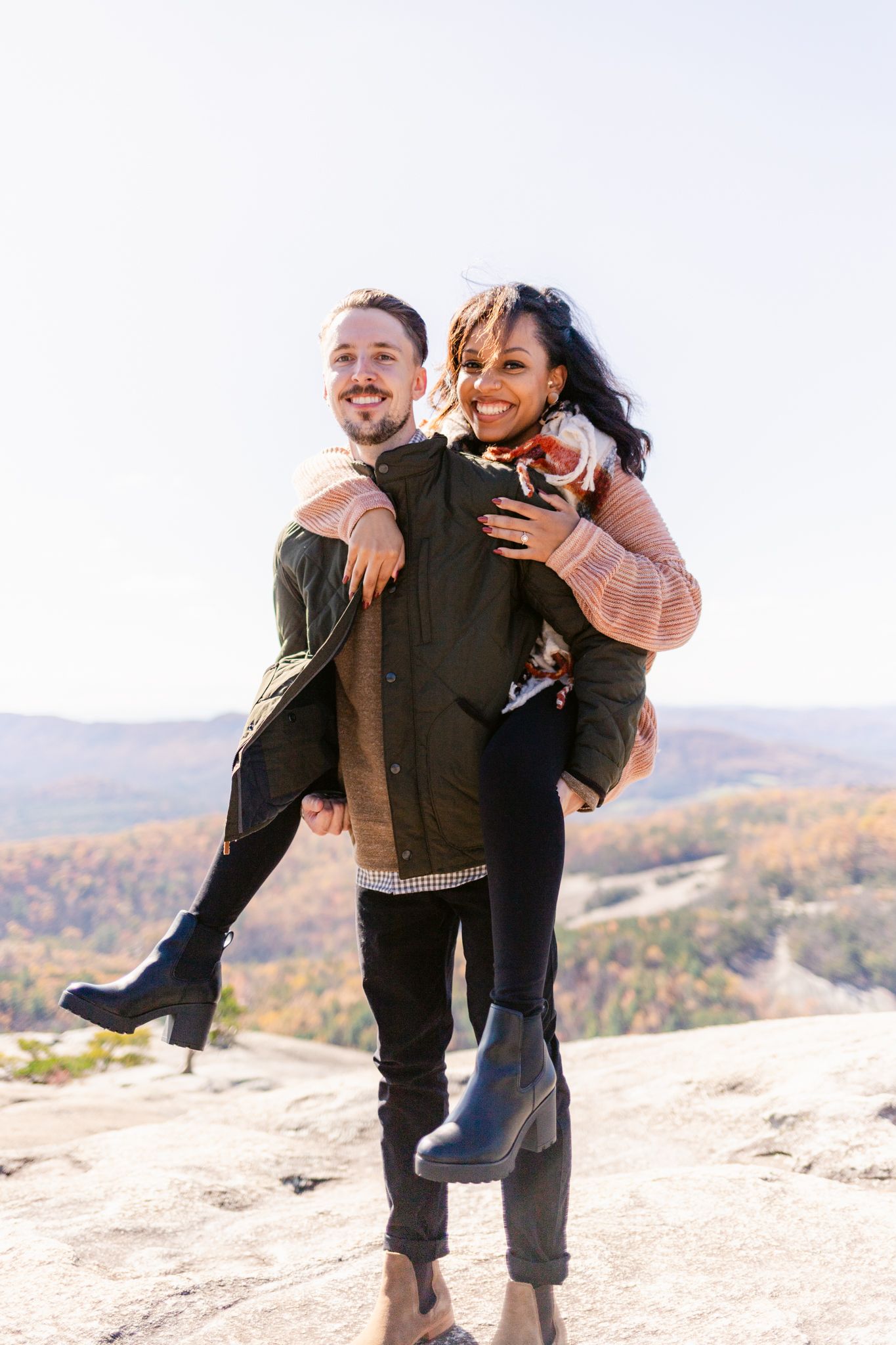 Two people laugh and embrace while enjoying a scenic mountain vista on a bright autumn day.