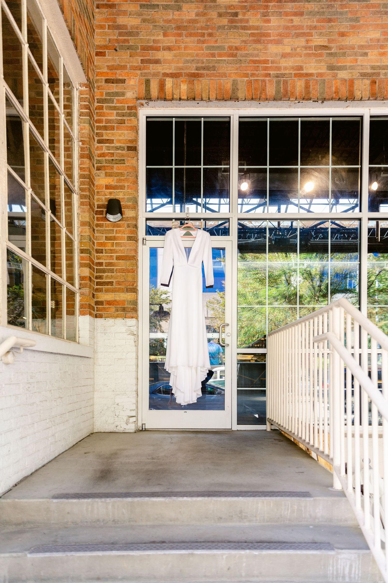 A covered brick walkway with white pillars and railings displays hanging white dresses along the storefront windows.