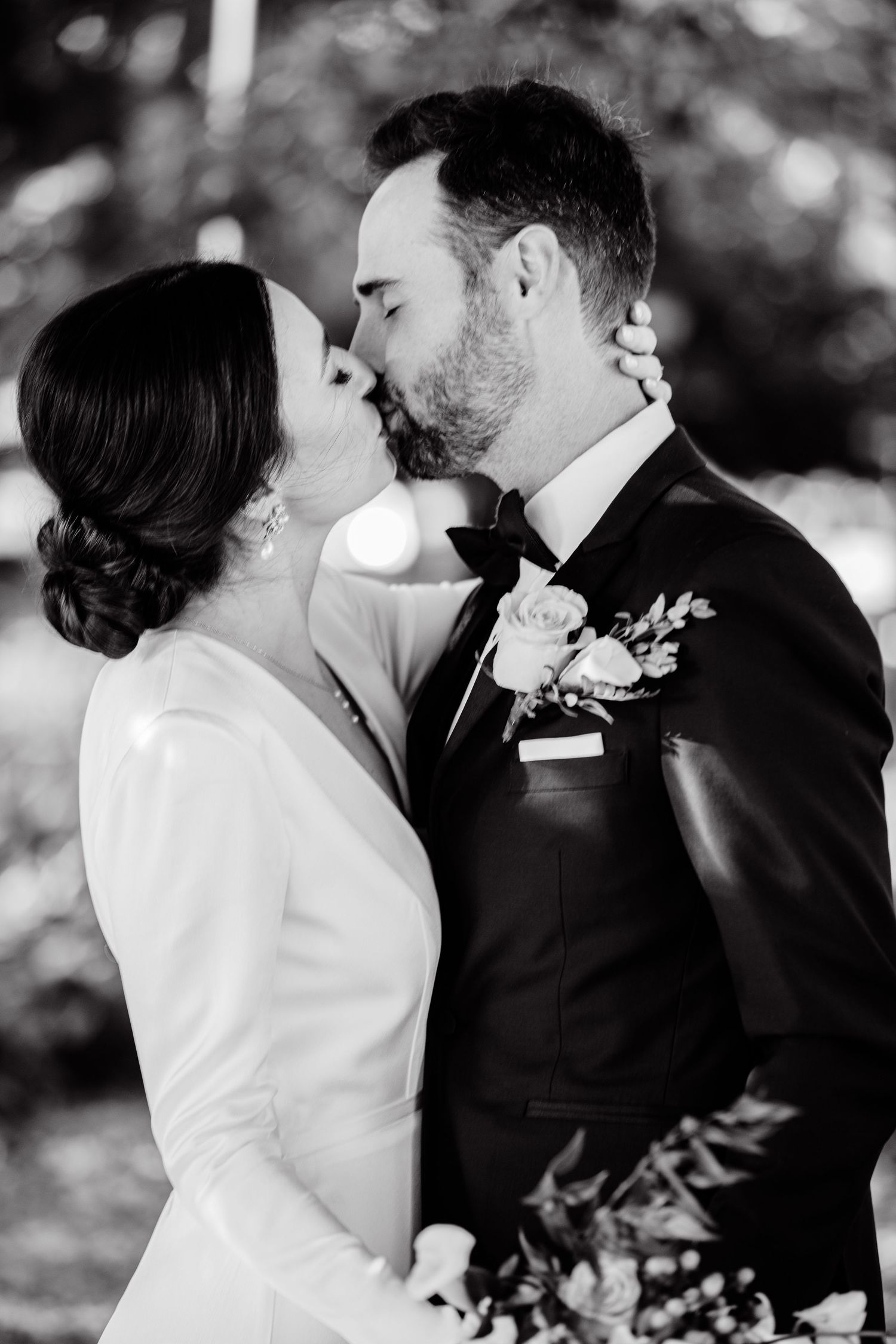 An intimate black and white portrait of newlyweds sharing a romantic kiss outdoors.