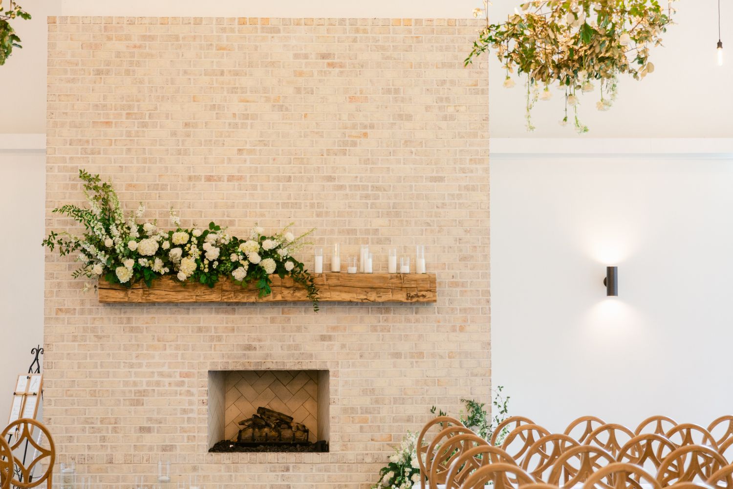 Modern wedding ceremony space with wooden chairs and a minimalist brick fireplace adorned with floral arrangements.