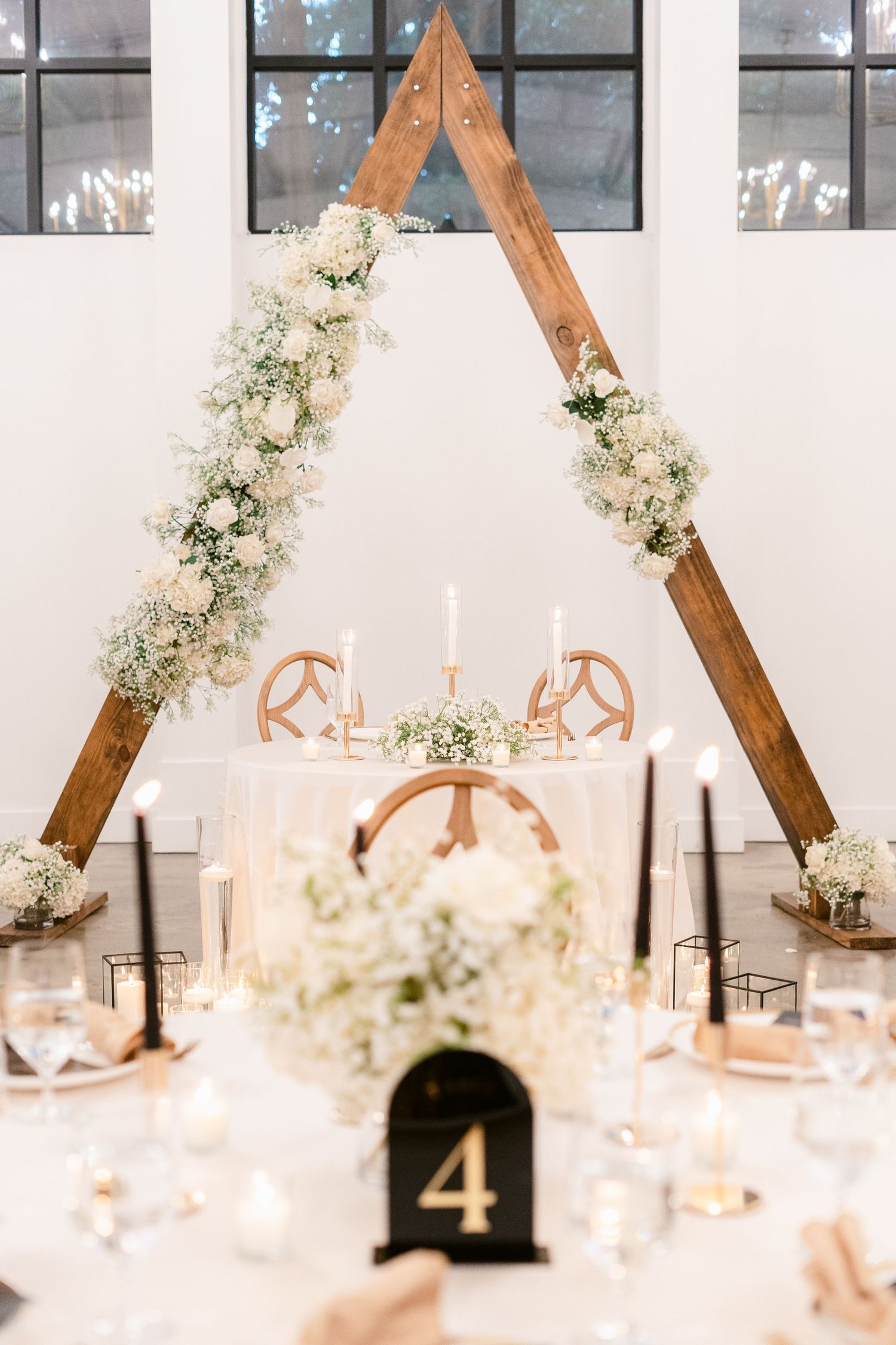 Elegant wedding table setting with wooden triangle arch decorated with white flowers and a table number 4 centerpiece.