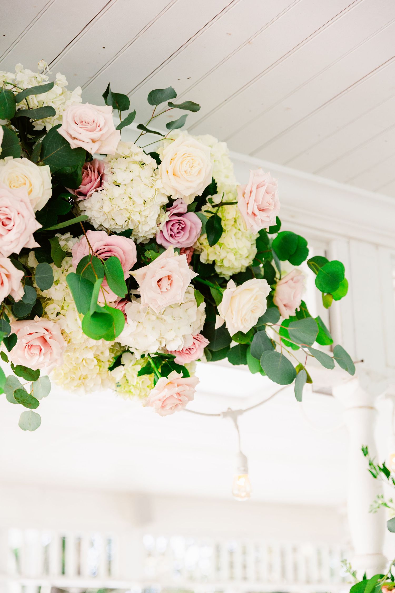 Romantic floral installation with pink roses and eucalyptus adorning a white ceiling beam in an event space.