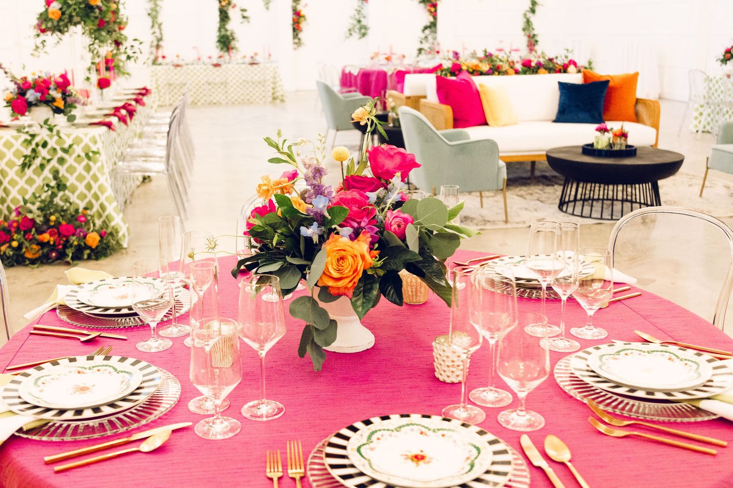 Wedding reception table settings with pink linens and striped plates decorated with colorful flowers.