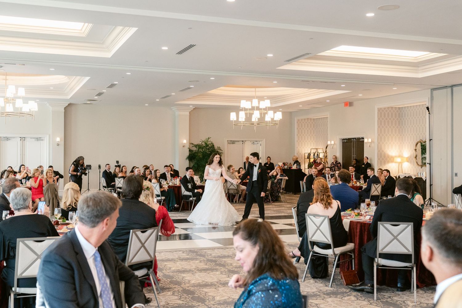 A panoramic view of a formal event space with guests seated at round tables in an elegant white room.
