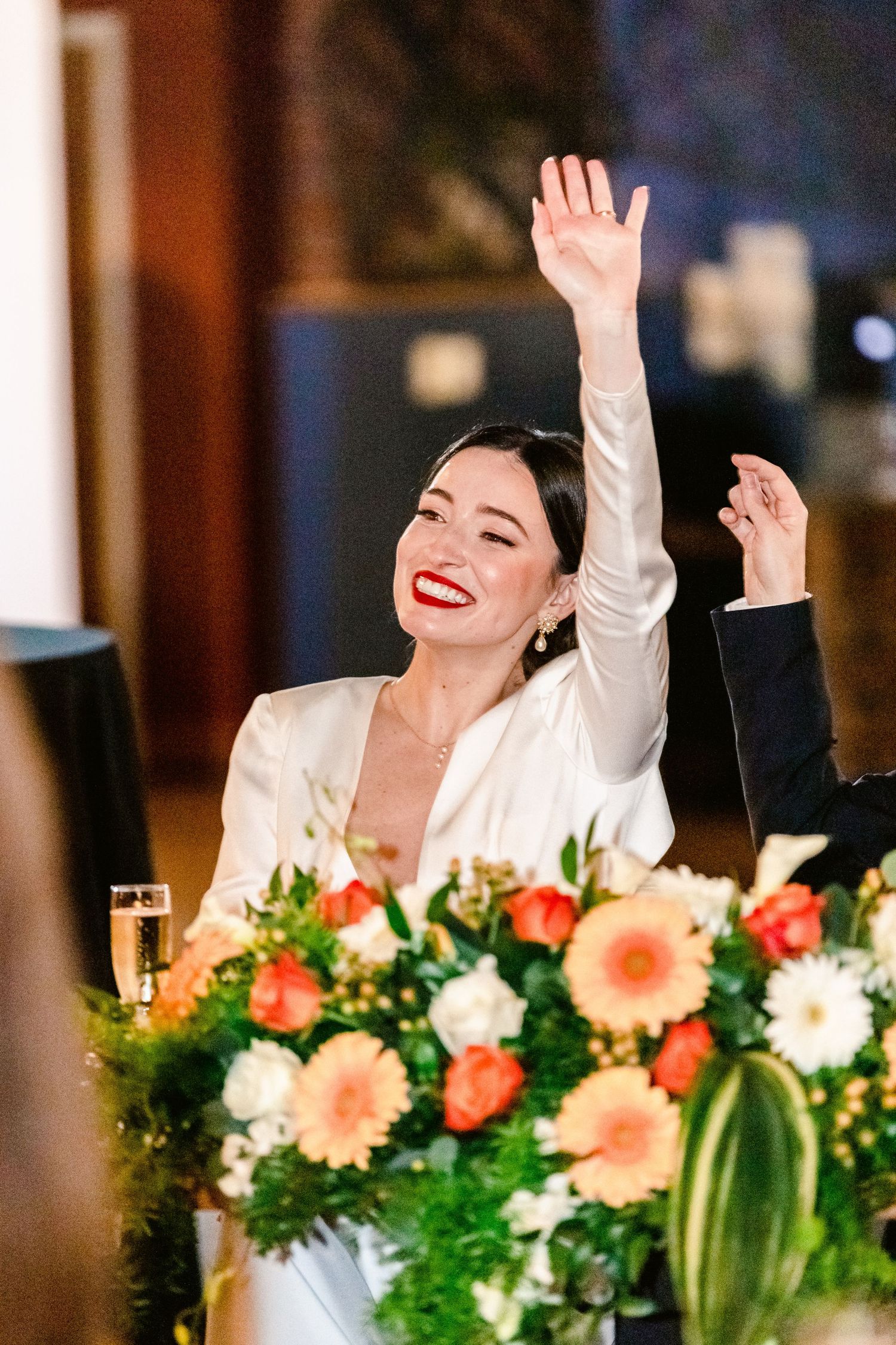 A person in a white top laughs joyfully at a reception table decorated with peach and green floral arrangements.