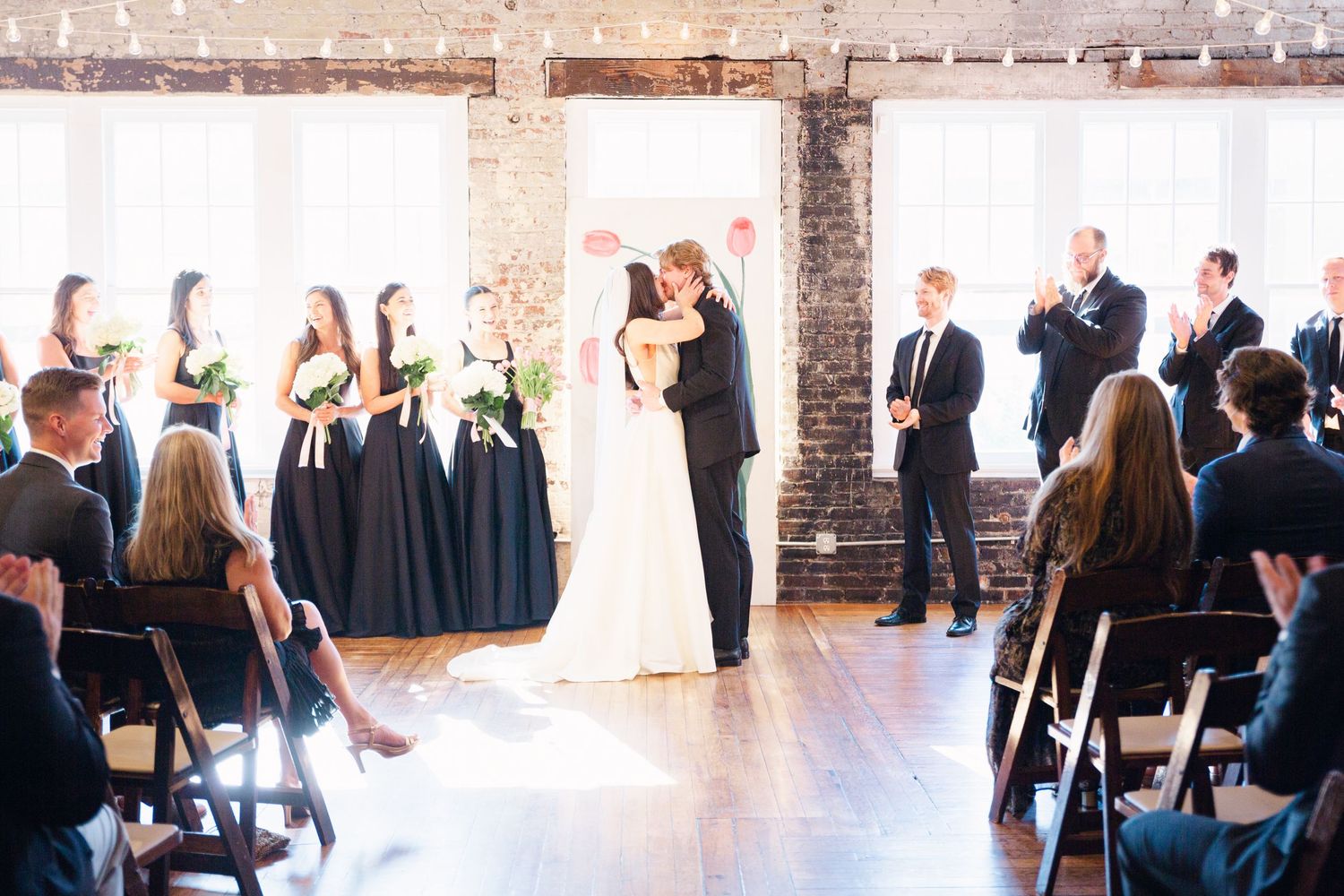 Wedding ceremony in industrial venue with exposed brick and large windows.