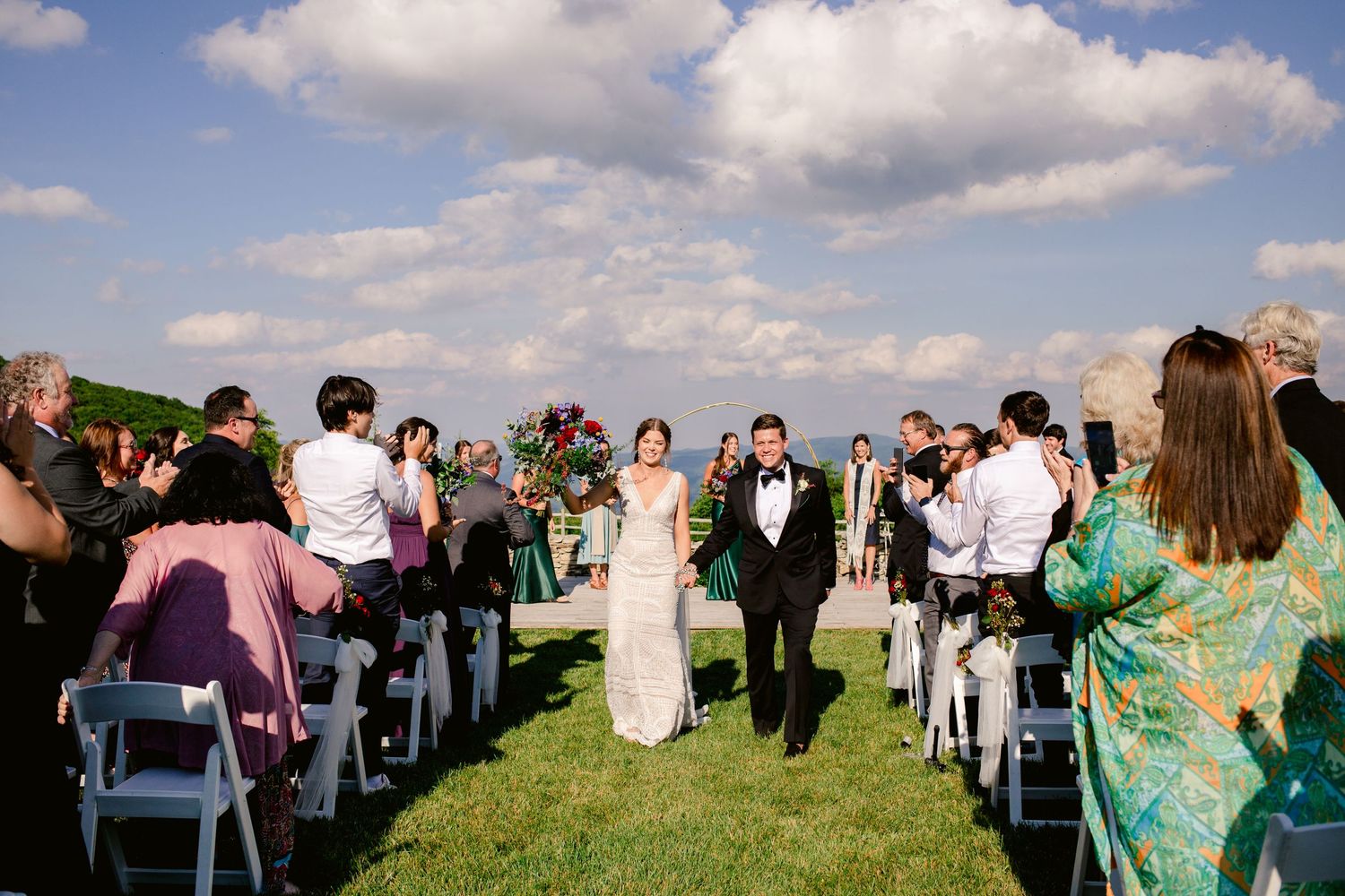 Newlyweds walking down the aisle as guests celebrate at outdoor mountain venue.