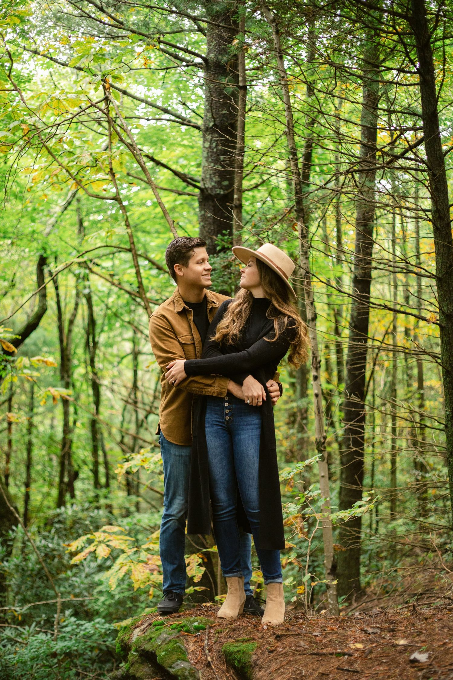 Couple embracing on a forest trail during autumn wearing casual attire.