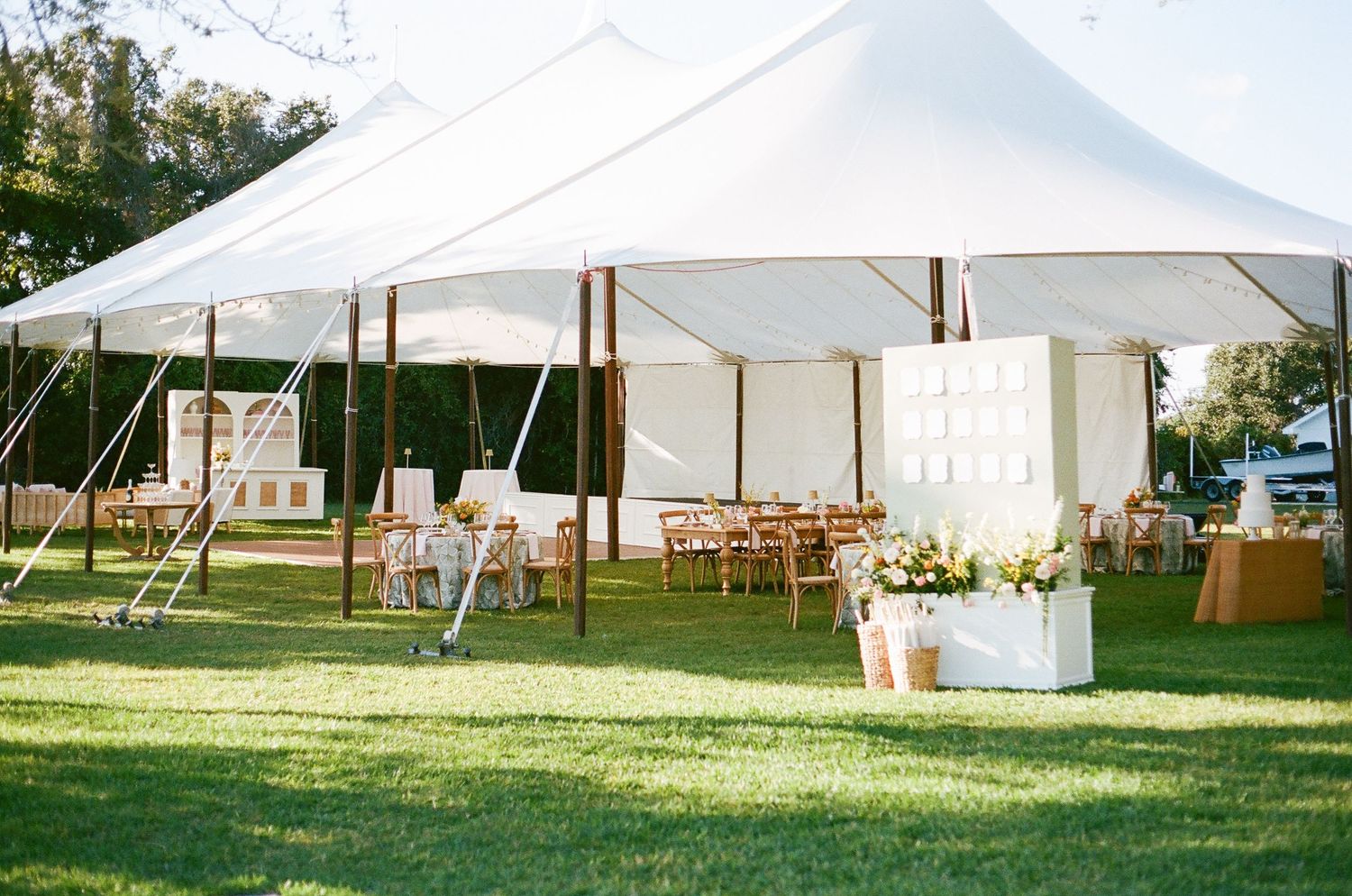 White wedding reception tent set up on a lush green lawn with wooden chairs and elegant decor details.