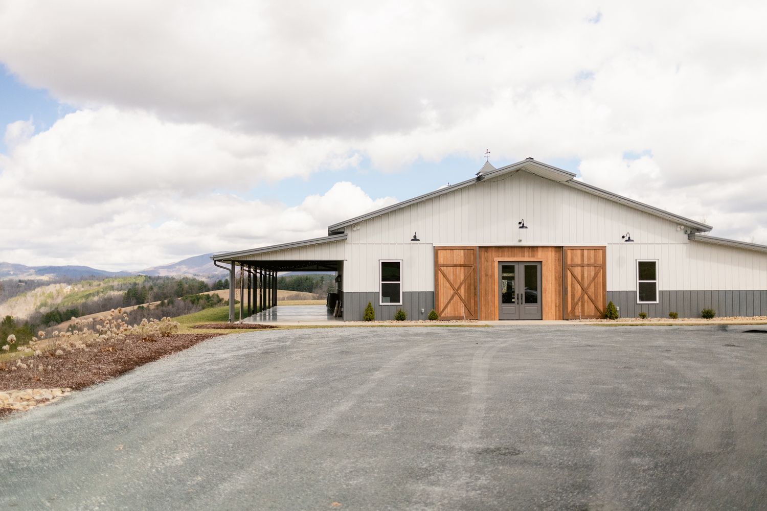 Modern industrial buildings with metal siding and wooden accents sit against a cloudy sky in a desert landscape.