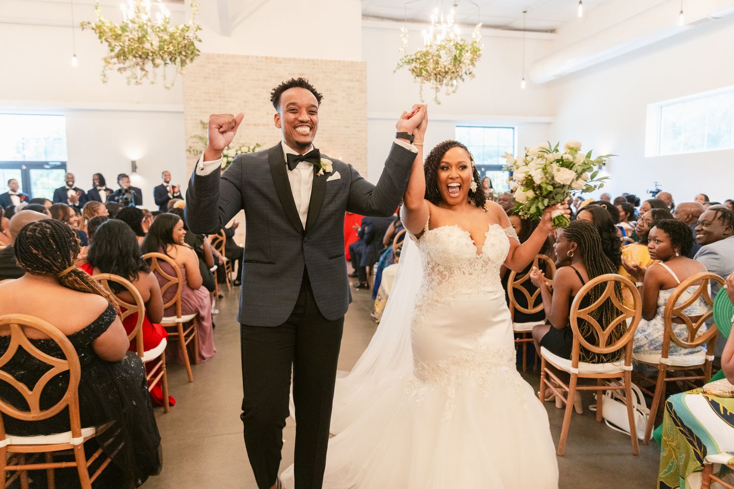 Newlyweds celebrate joyfully while walking down the aisle at their wedding ceremony in a bright modern venue.