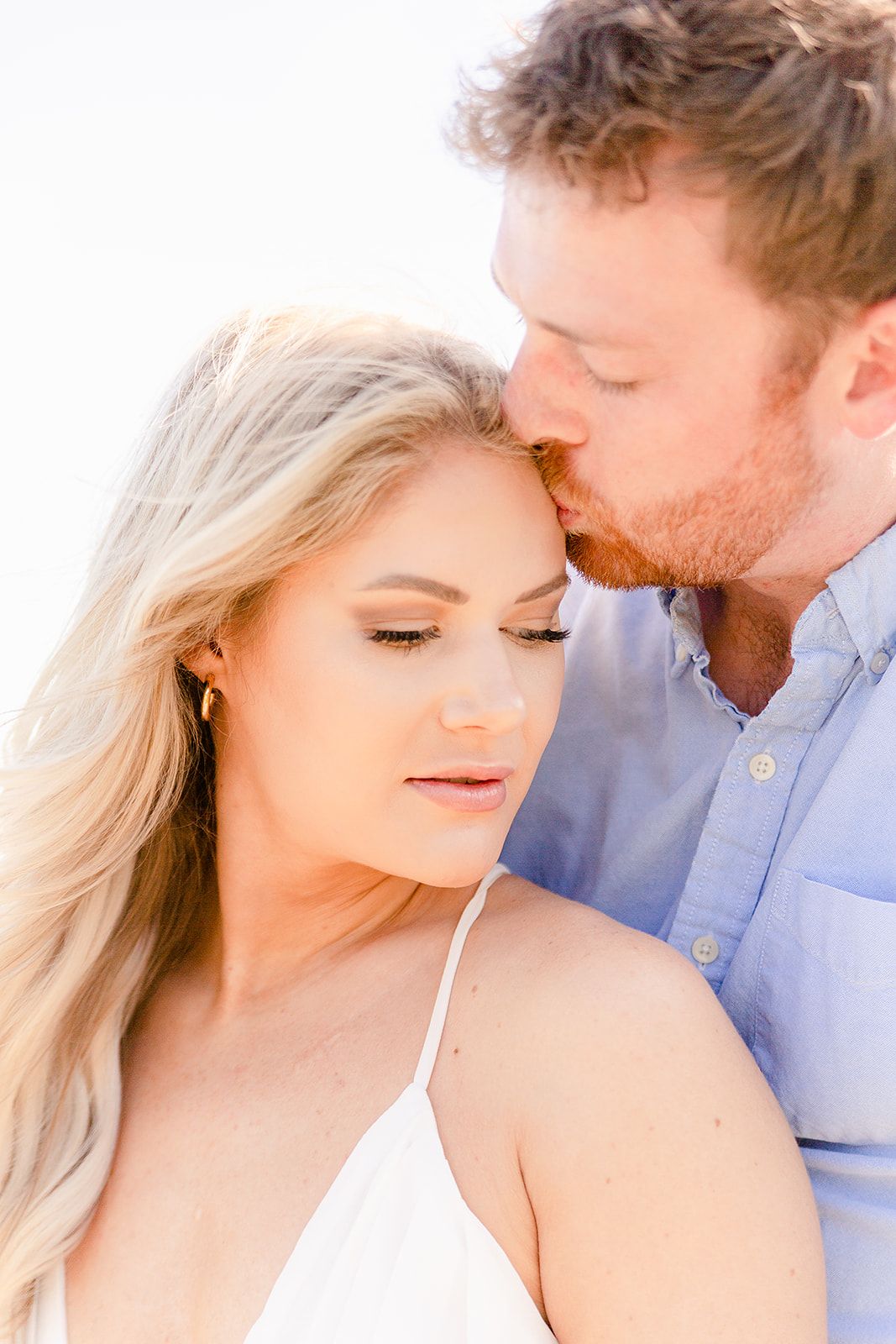 A romantic couple shares an intimate moment in warm sunlight, with her in white and him in blue.