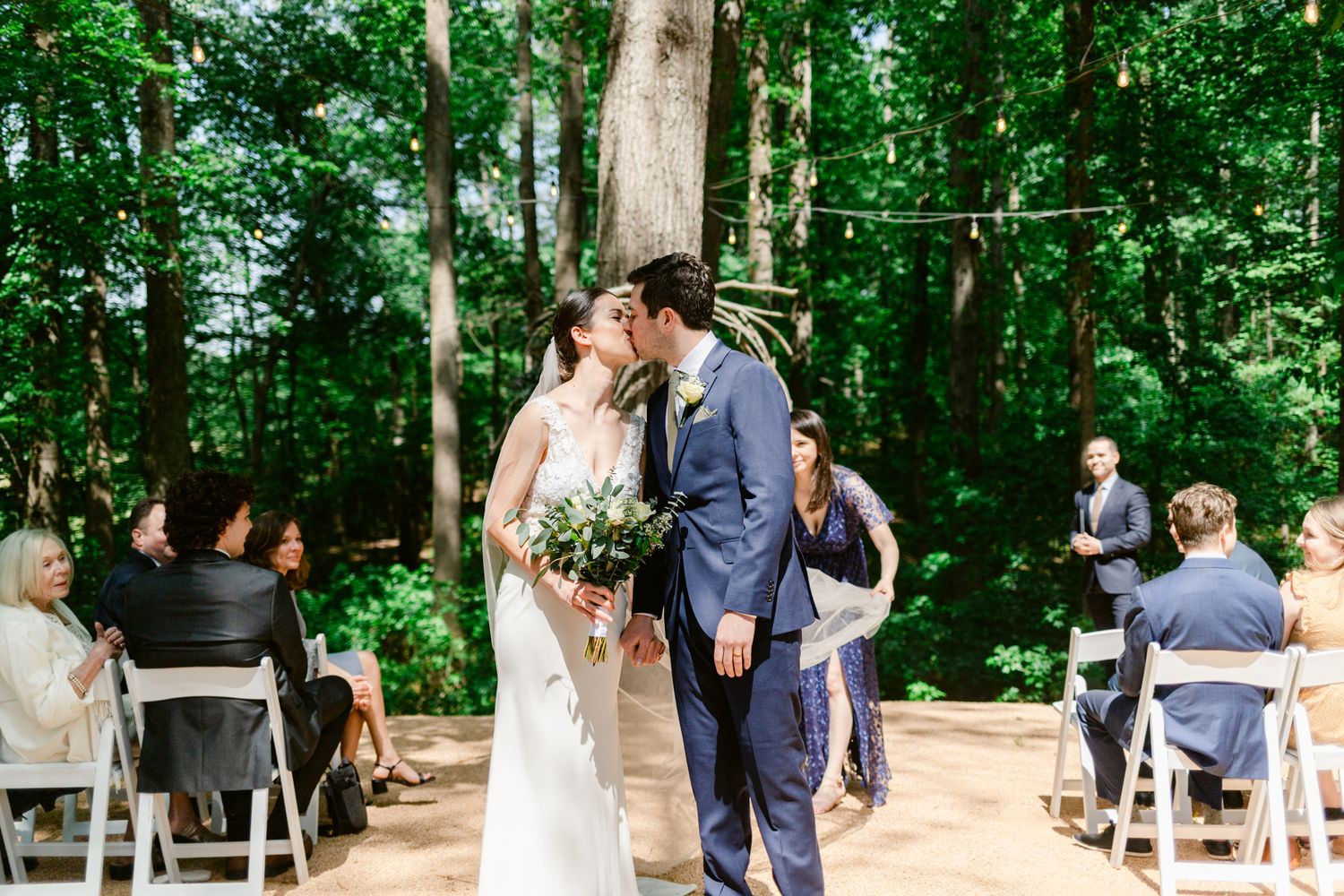 Panoramic view of an outdoor forest wedding ceremony with guests standing among tall trees.