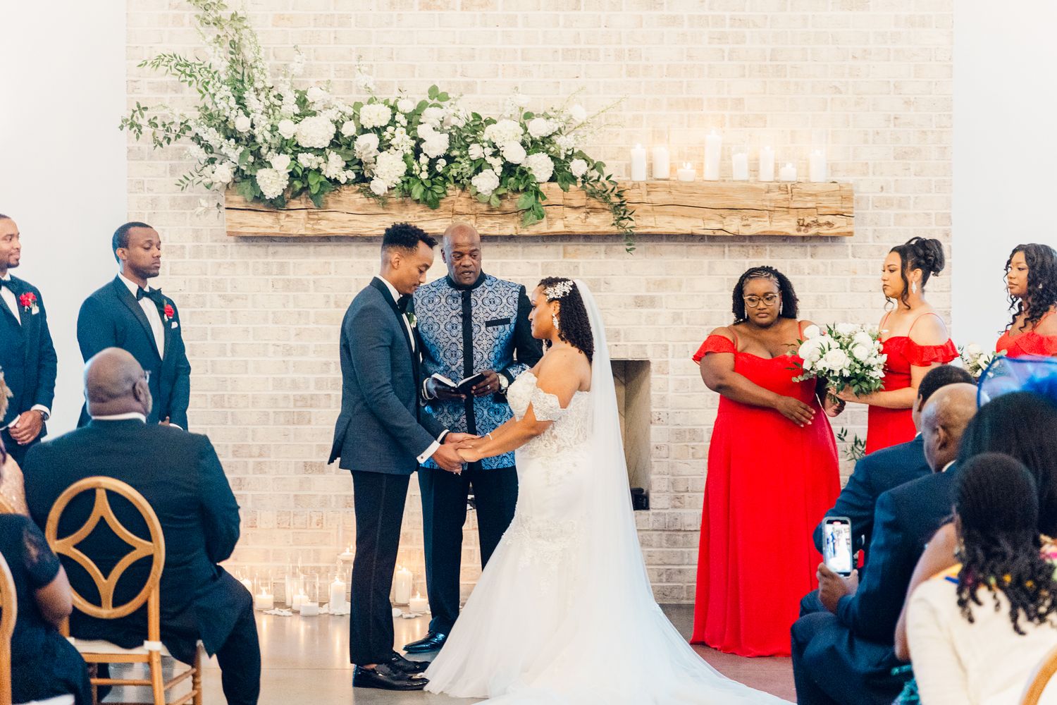 Wedding ceremony in a light-filled venue with bridesmaids in red dresses watching the couple exchange vows.