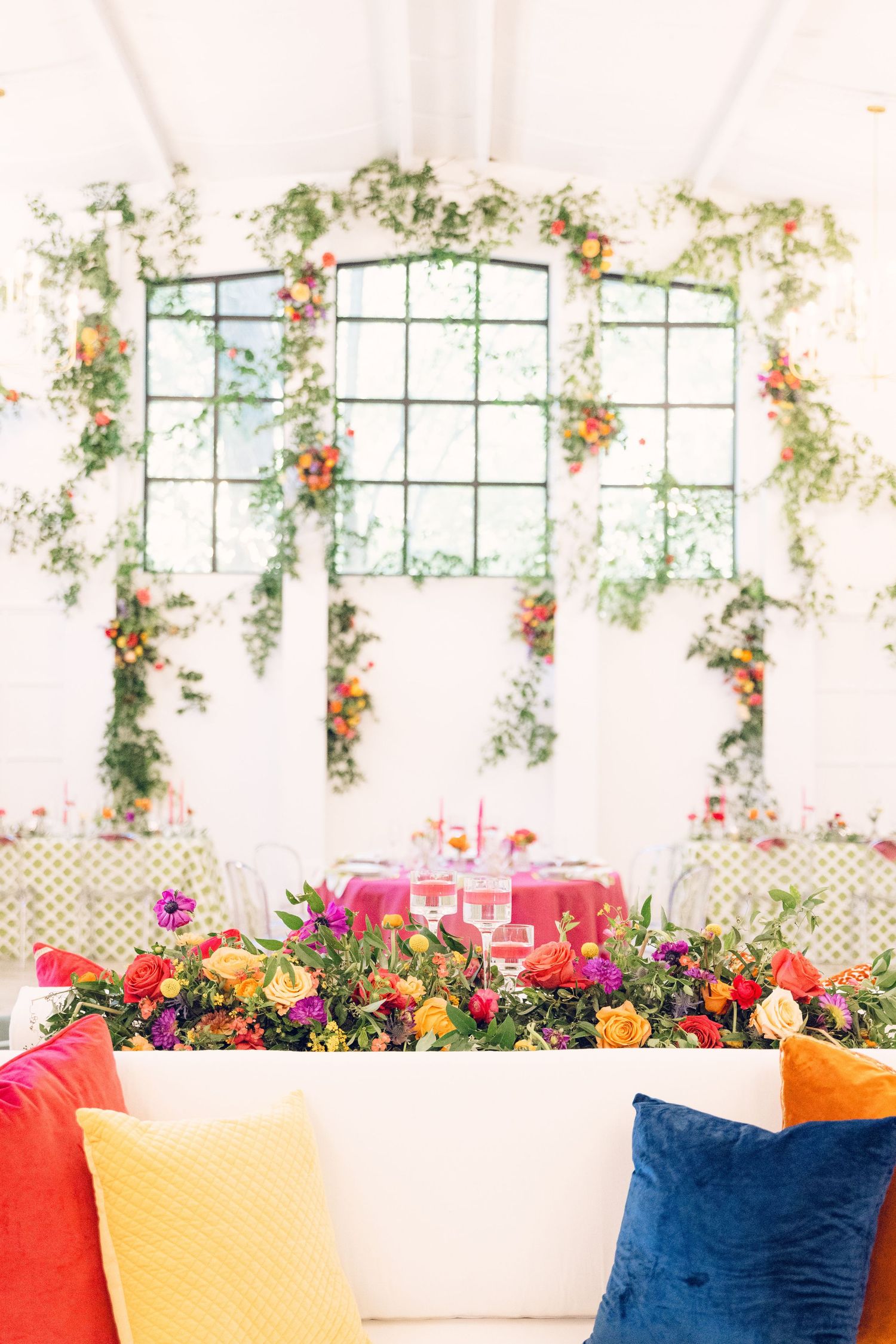 Bright reception space with navy and coral pillows under hanging floral installations.
