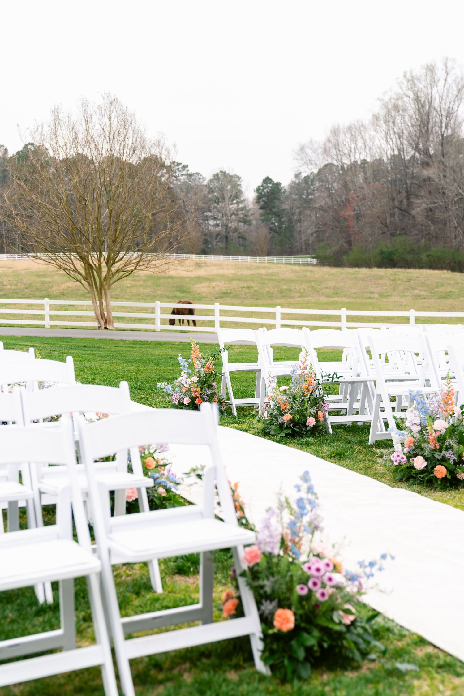 White folding chairs arranged in rows on a green lawn with colorful floral arrangements for an outdoor wedding ceremony.