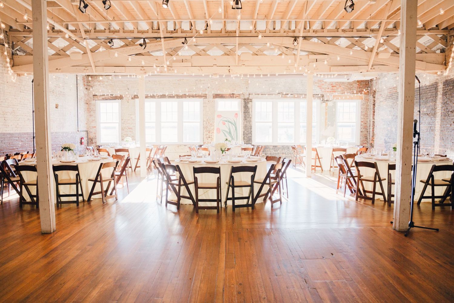 Rustic wedding venue with wooden floors, exposed brick, and folding chairs set for ceremony.
