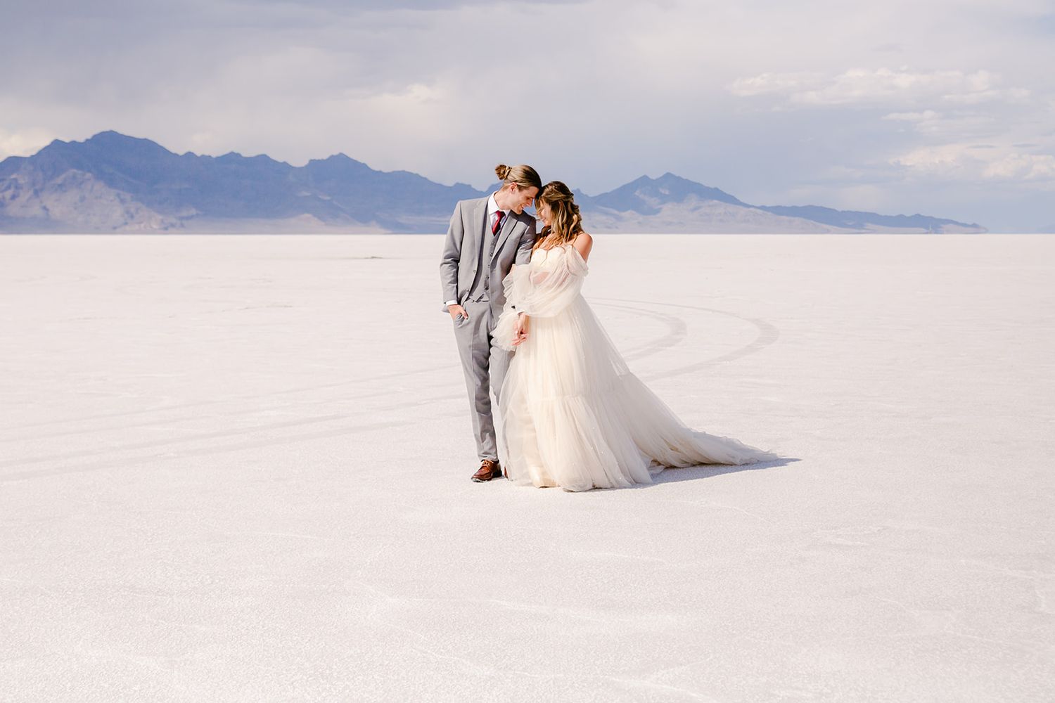 Bride and groom embrace on the vast white salt flats with mountain backdrop on their wedding day.