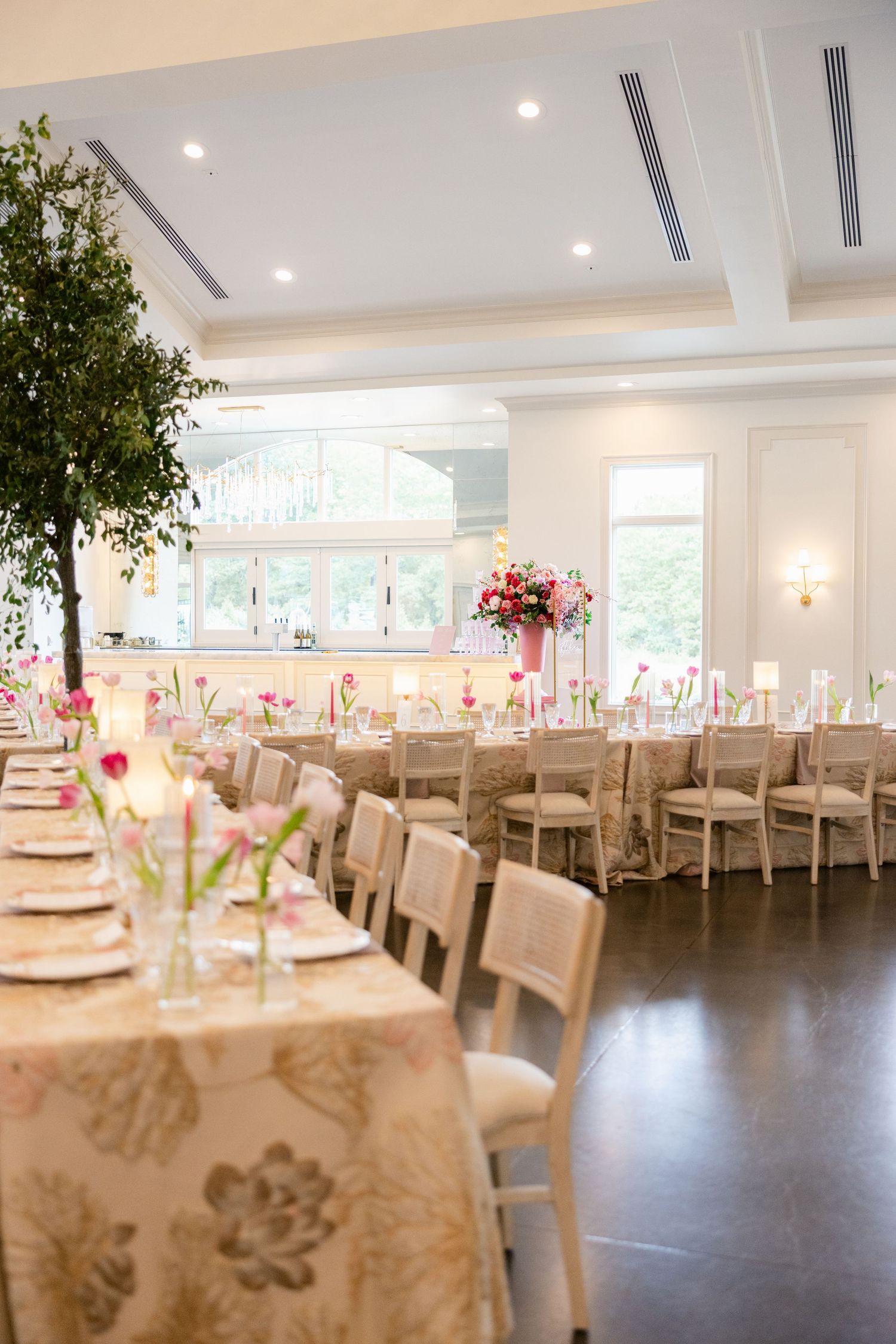 Elegant wedding reception room with white chairs and pink floral table settings.