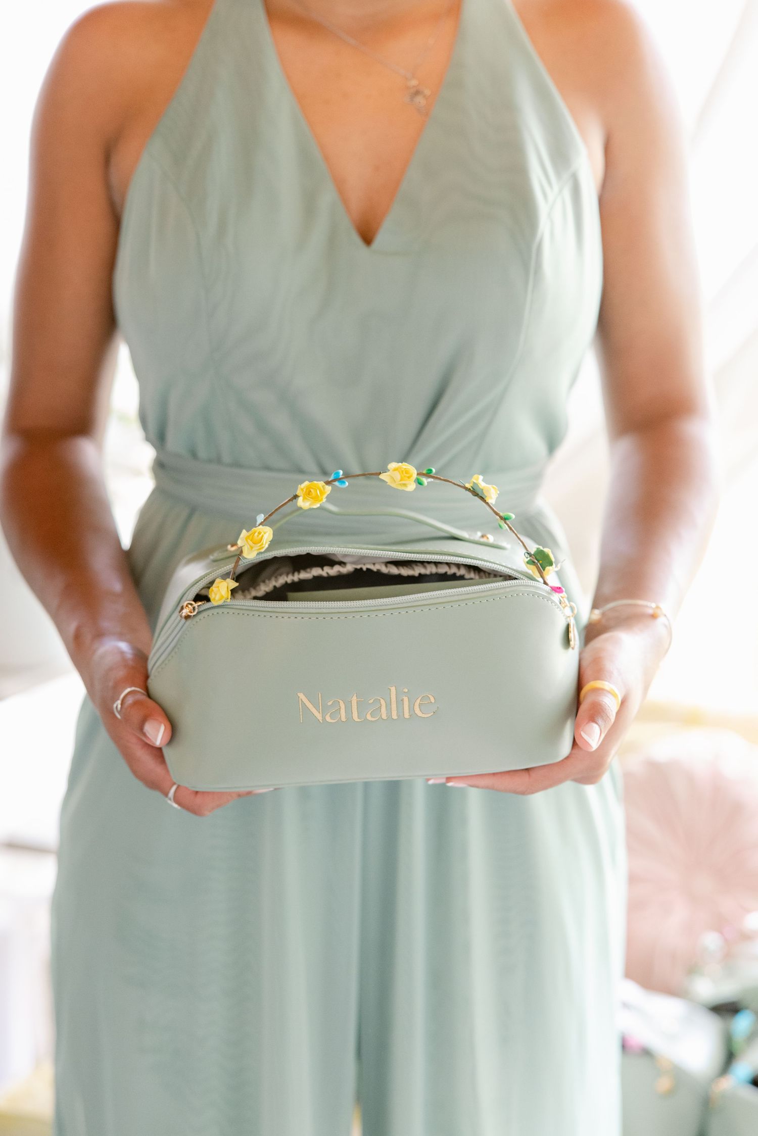 Bridesmaids in sage green dresses holding matching sage-colored gift boxes with gold accents.