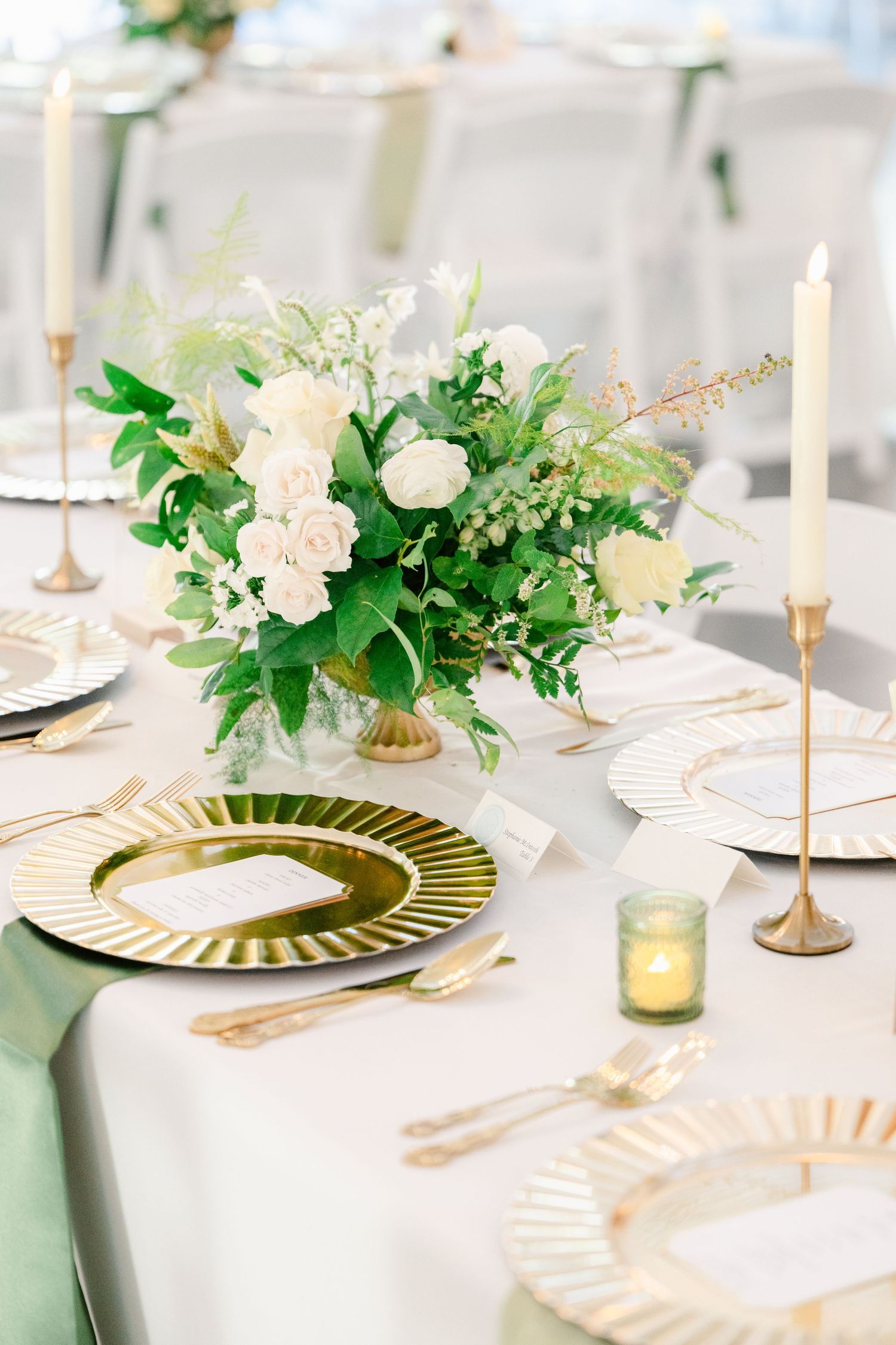Elegant white and gold table settings with fresh floral centerpieces and taper candles create a sophisticated dining atmosphere.