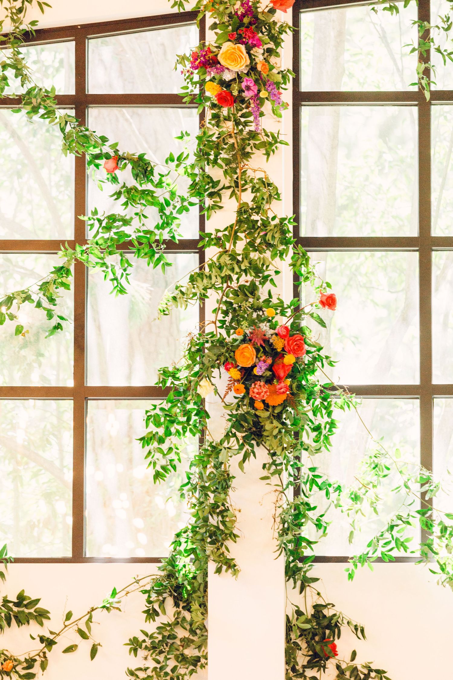 Colorful floral arrangements with orange and red blooms cascade down white lattice panels in an elegant indoor setting.