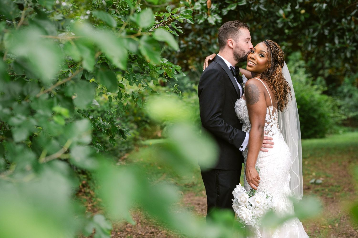 A romantic wedding couple embraces in a lush green garden setting during their outdoor photo session.