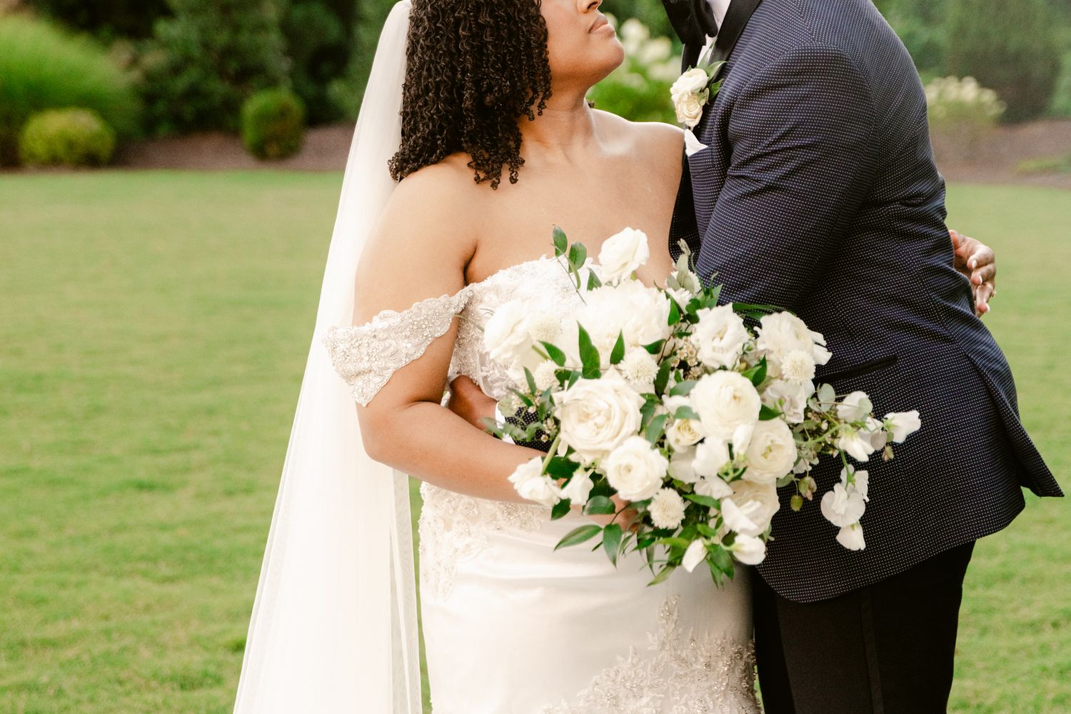A couple shares an intimate moment on their wedding day in a lush garden setting with white floral bouquet.