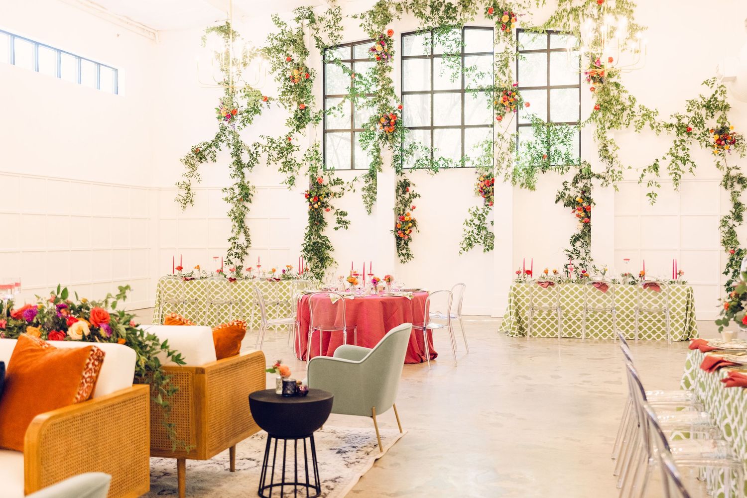 Modern event space with greenery draped windows and orange accent furniture.