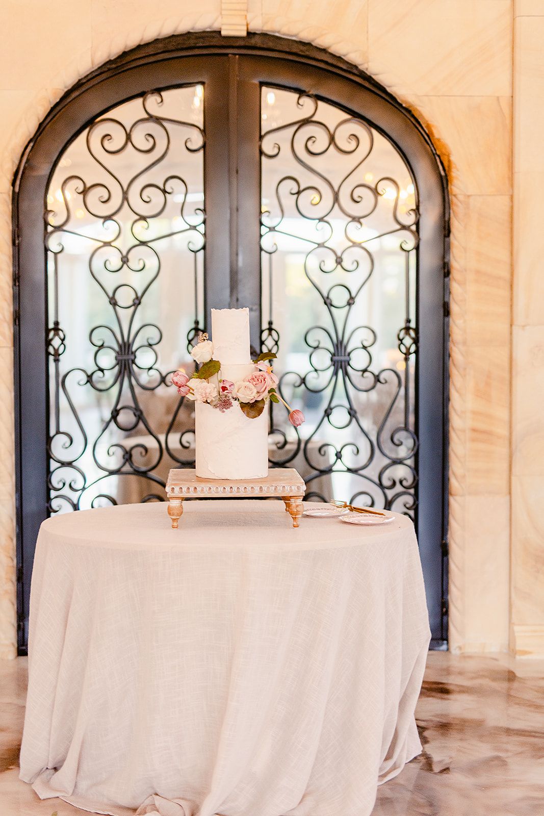 White tablecloths and floral arrangements displayed against ornate wrought iron window details in event space.