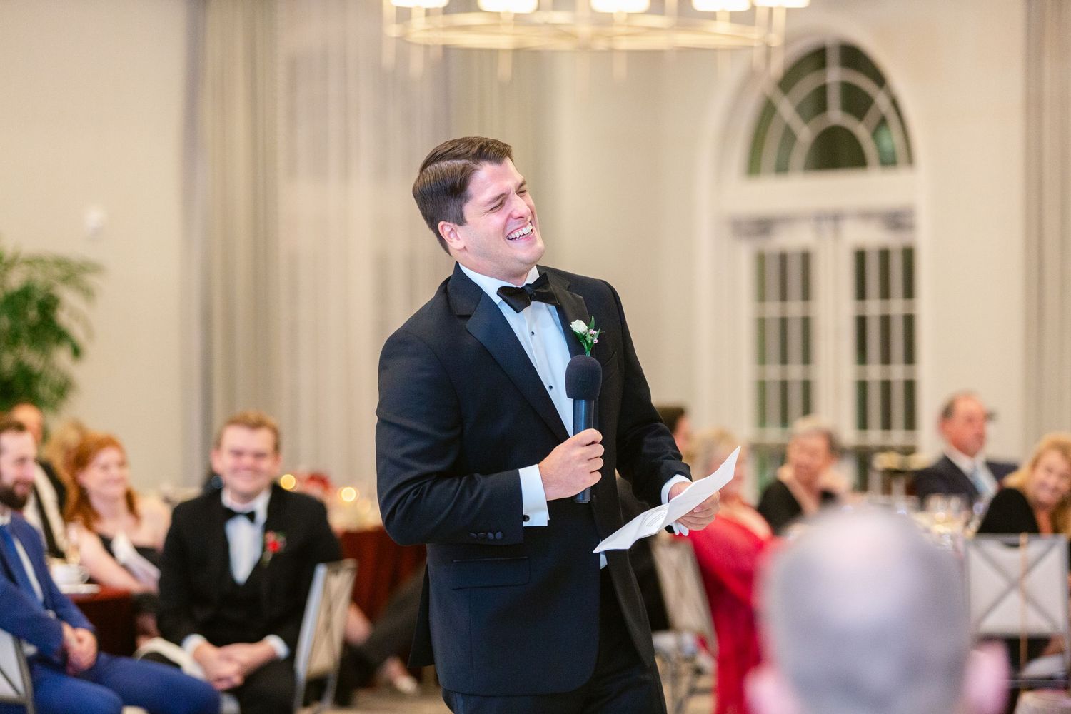 Wedding guests dancing and socializing at an elegant reception with crystal chandeliers and white decor.