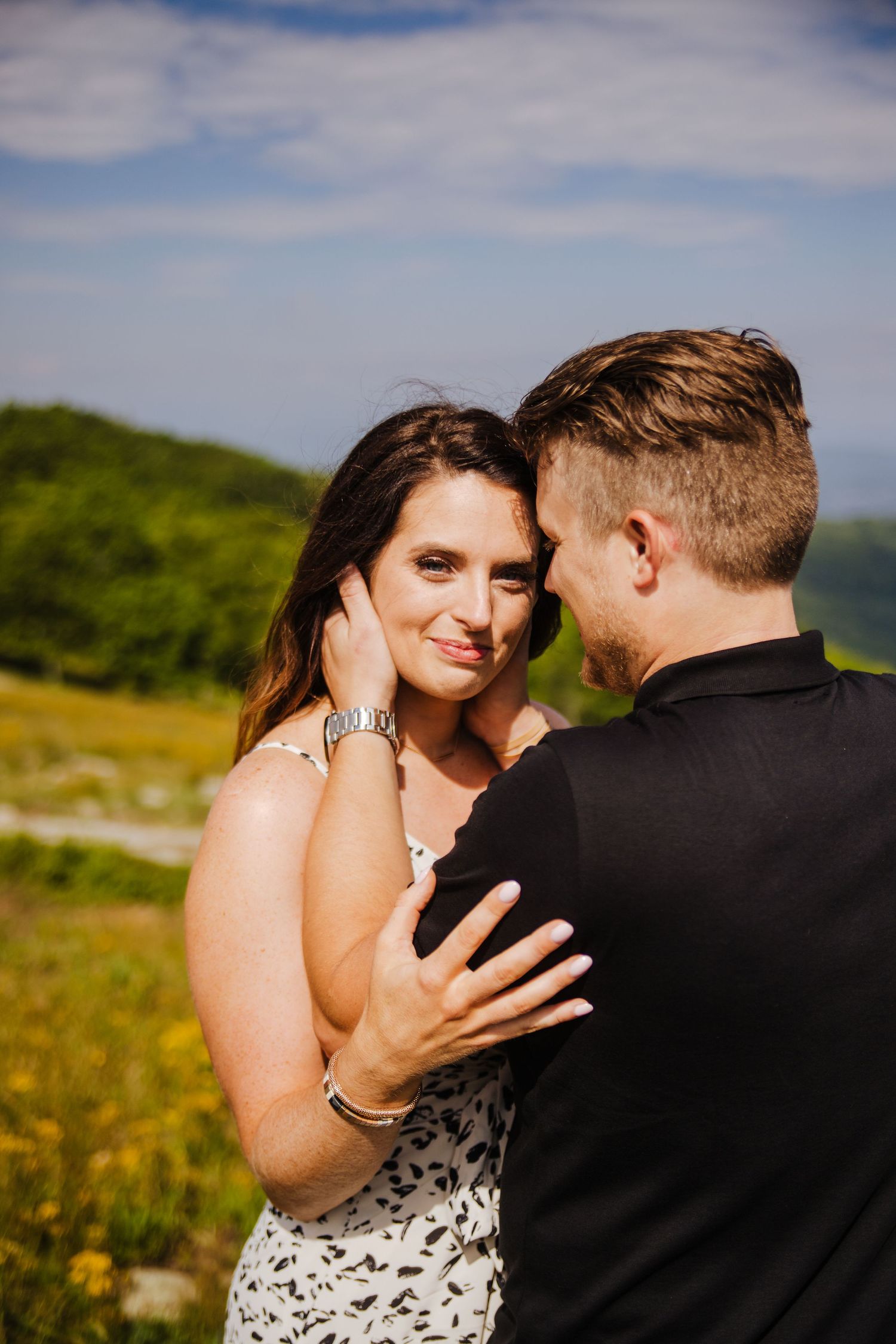 Intimate moment between couple in casual attire against mountain backdrop with wildflowers.