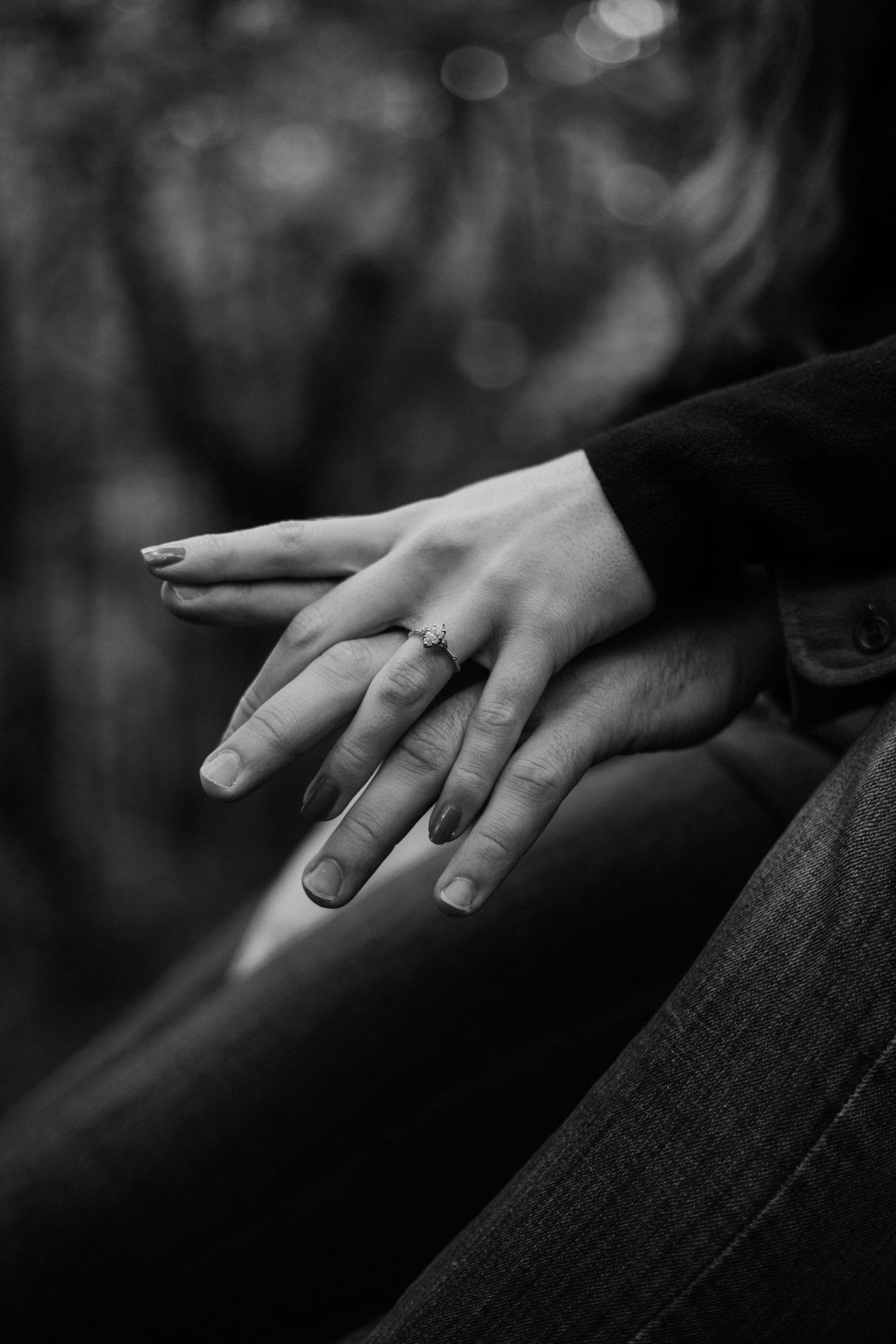 Close-up black and white photo of hands with an engagement ring against a blurred background.