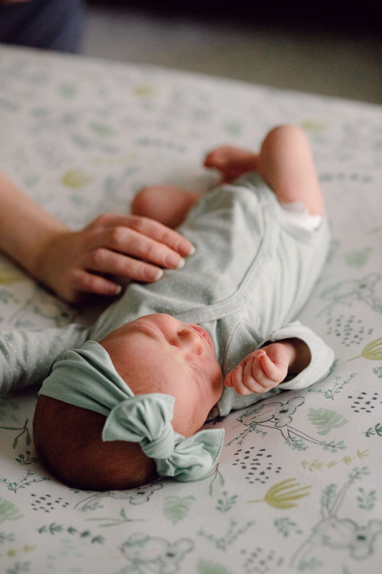 Newborn baby resting on floral patterned fabric wearing mint green clothing.