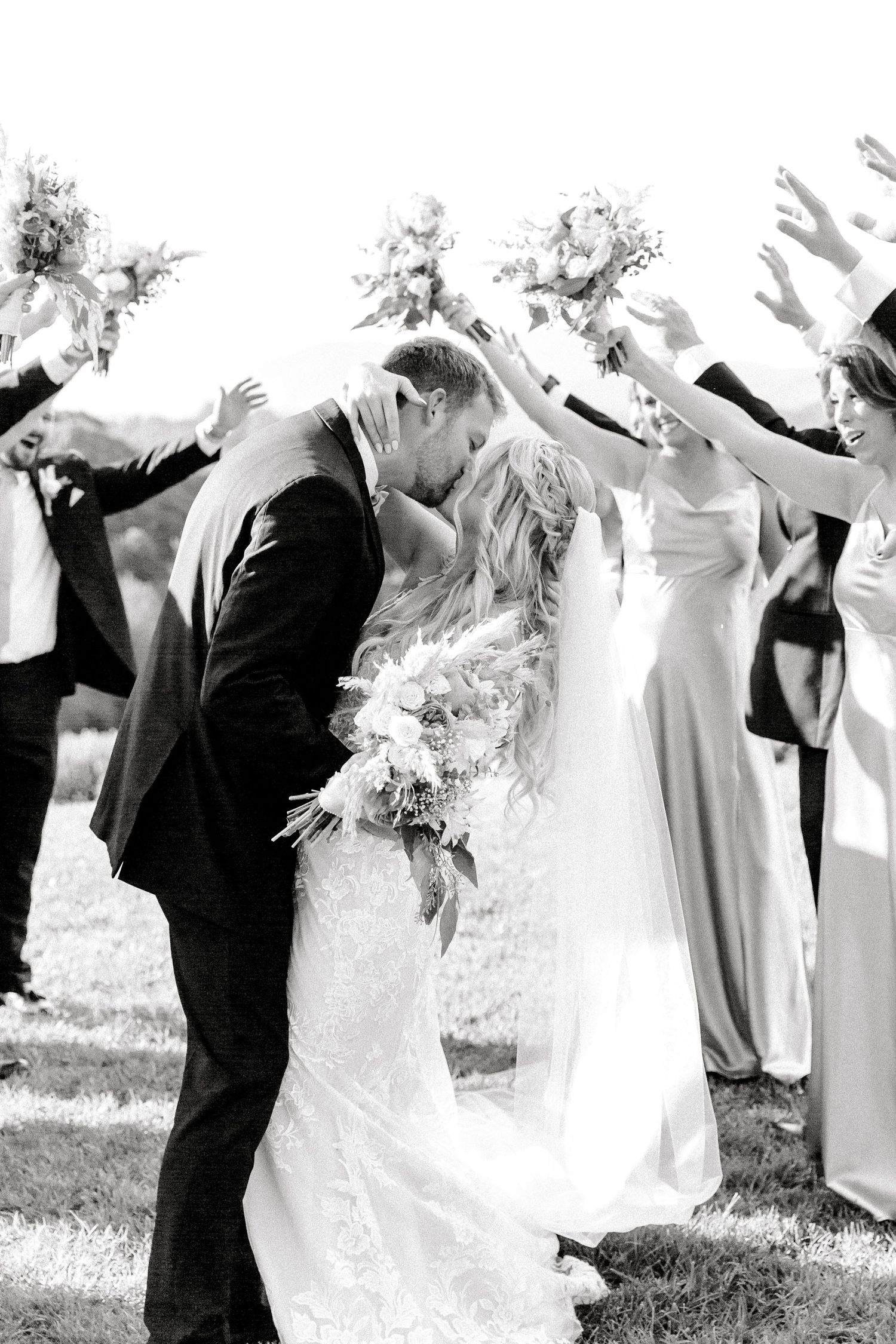 Black and white wedding photo series showing joyful celebration with dancing and embracing couples in formal attire outdoors.