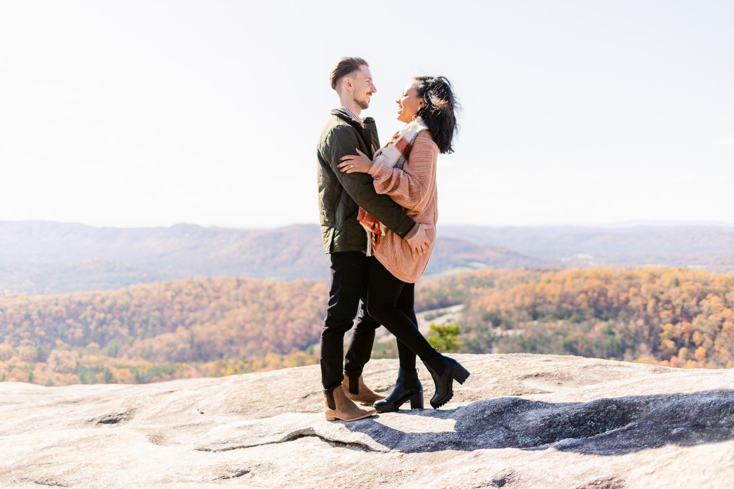A couple dances together on a mountain summit overlooking a scenic autumn valley landscape at sunset.