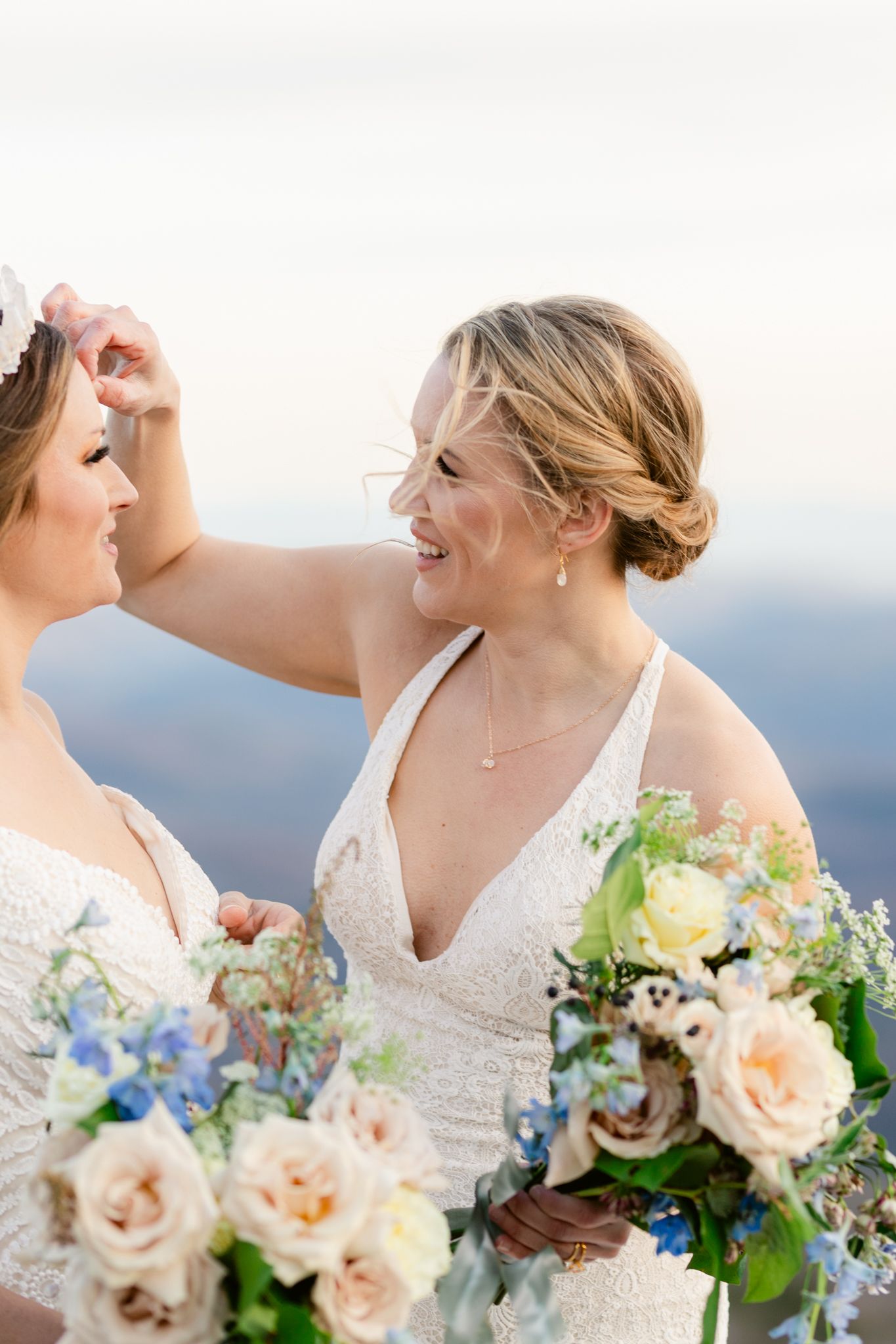 A romantic wedding couple shares intimate moments while holding peach and blue floral bouquets against a scenic backdrop.