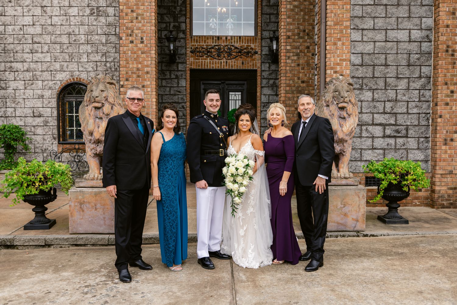 Wedding party members pose in front of a rustic brick building exterior during a formal celebration.