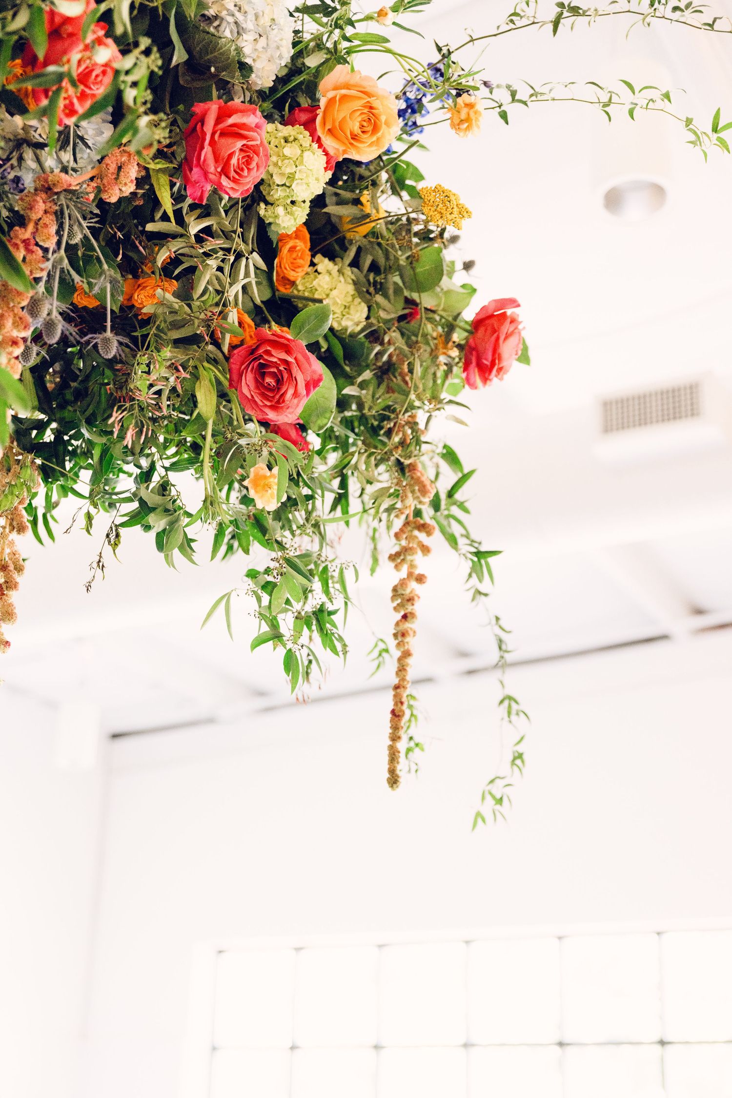 Hanging floral arrangement with coral roses, orange blooms and cascading greenery against a white ceiling.