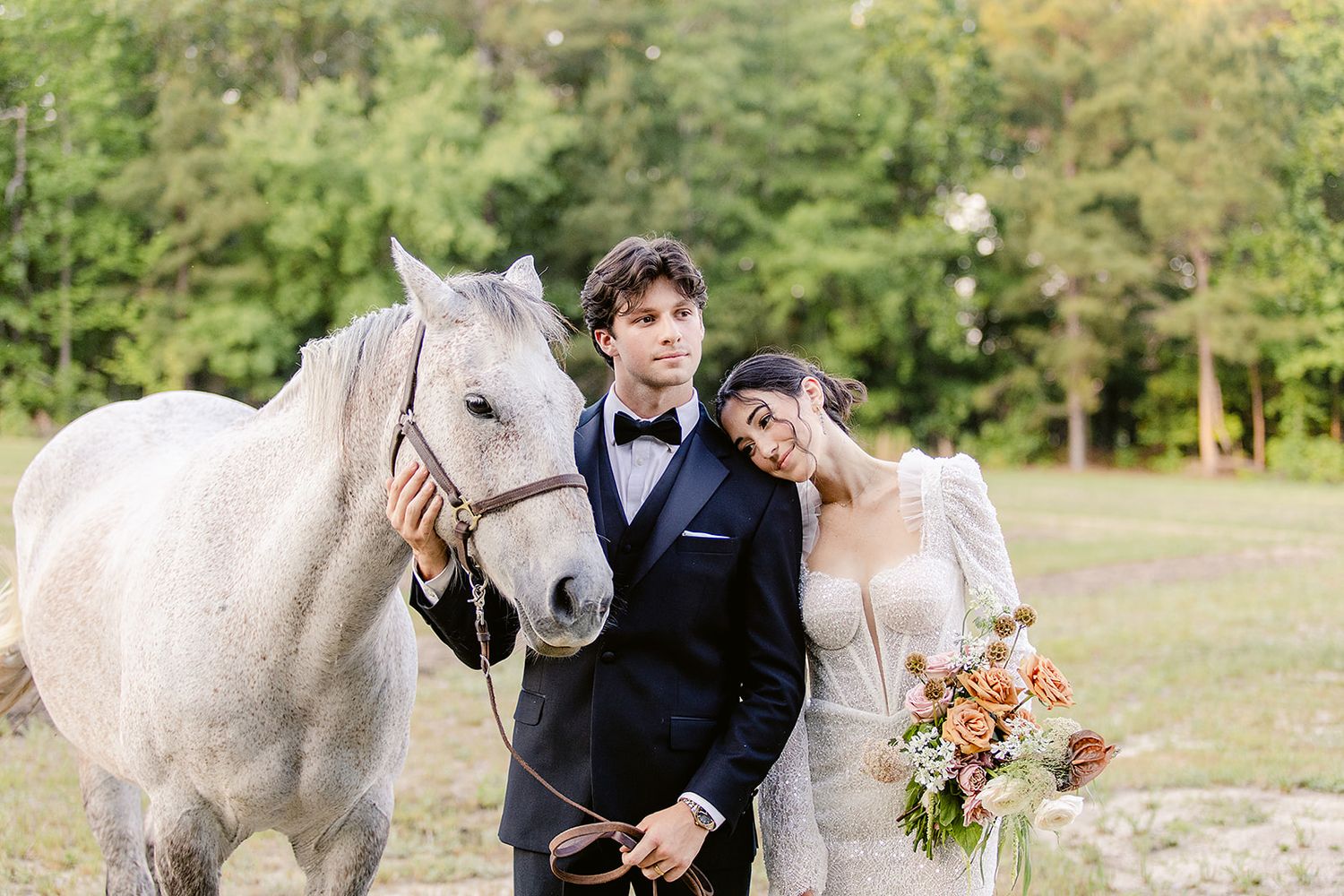 A wedding couple shares intimate moments with a beautiful white horse in a scenic outdoor setting.