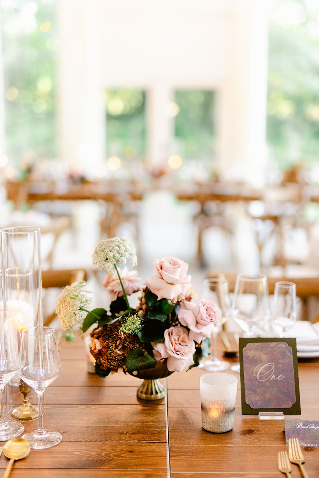 Rustic wooden table decorated with pink roses, place settings and romantic candlelight for a wedding reception.
